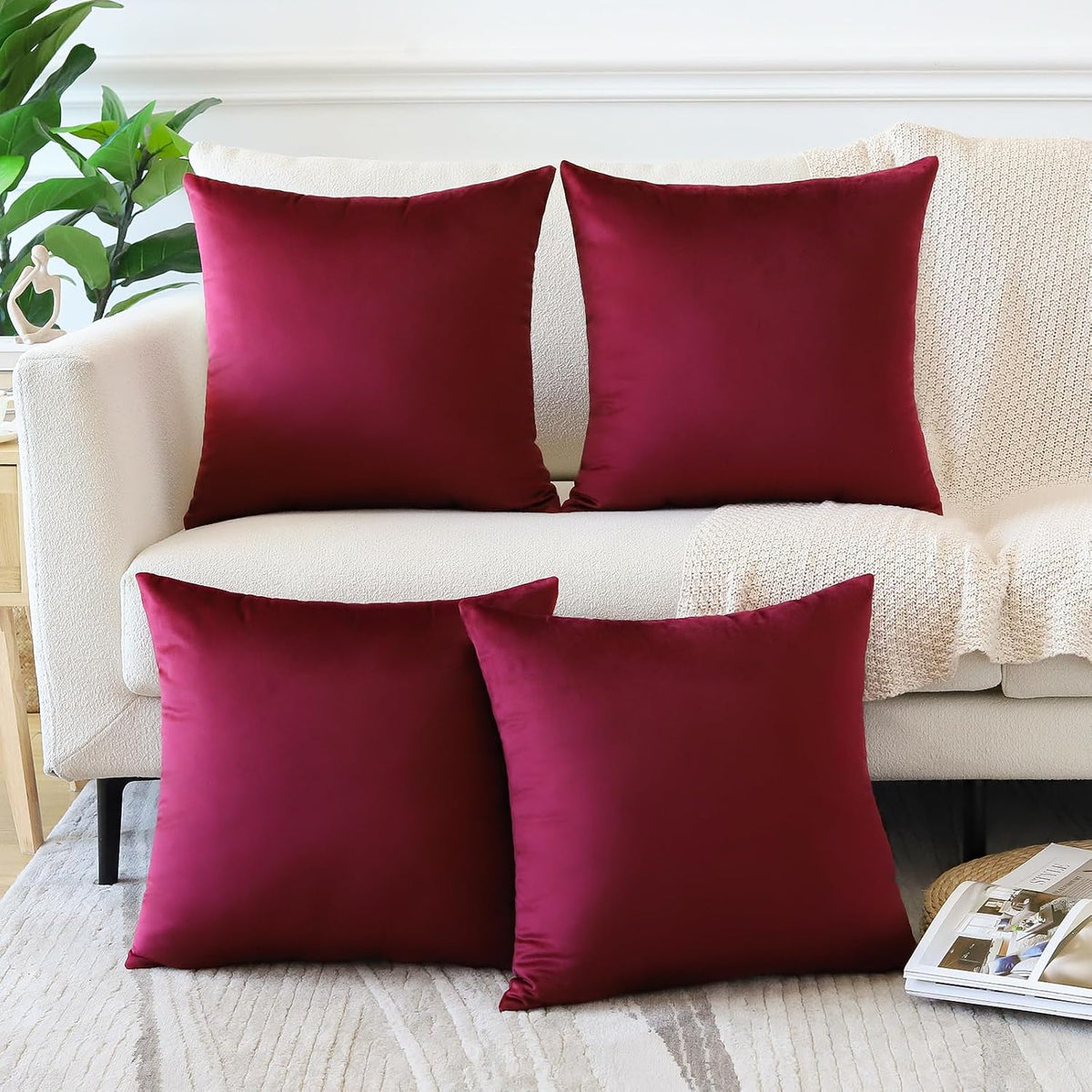 Four square velvet pillow covers in deep burgundy arranged on a cream sofa and rug.