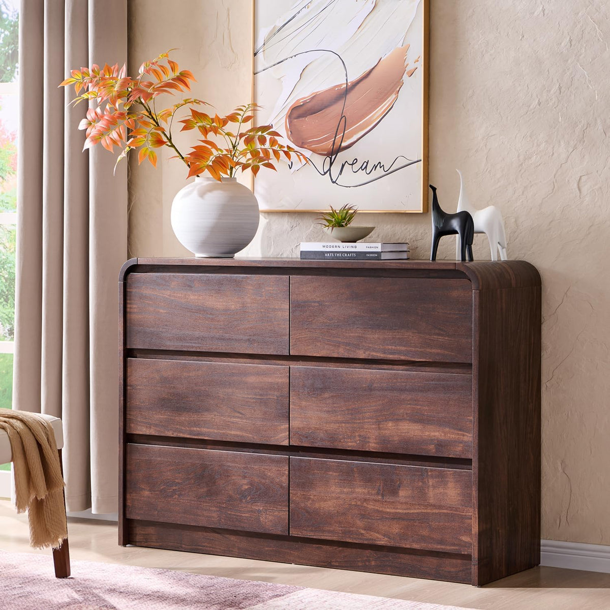 Low six-drawer dresser in a warm dark brown finish styled with vase and art on top in a softly lit bedroom