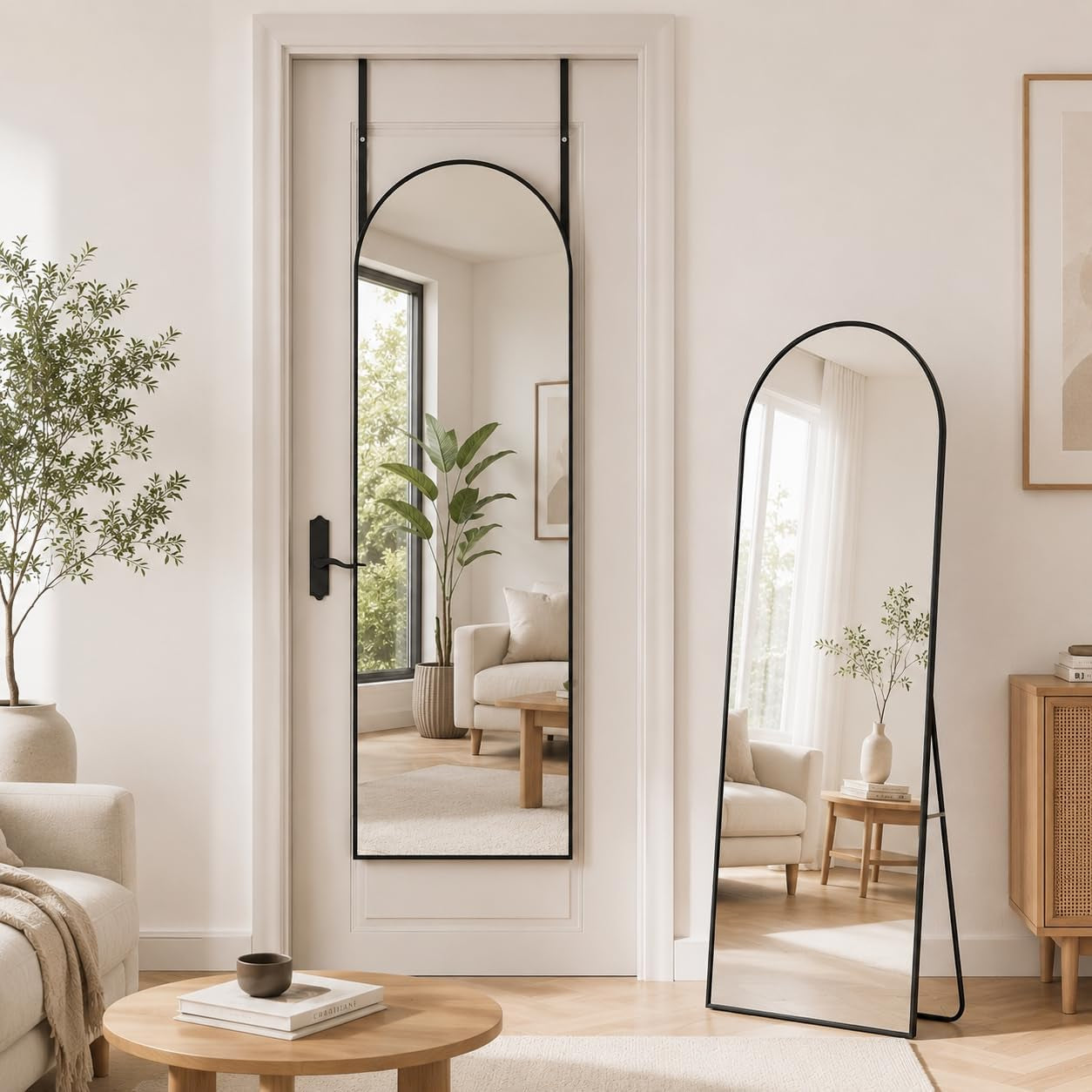 Two arched full-length mirrors with slim black frames: one hung on a door, one freestanding and leaning beside a sideboard