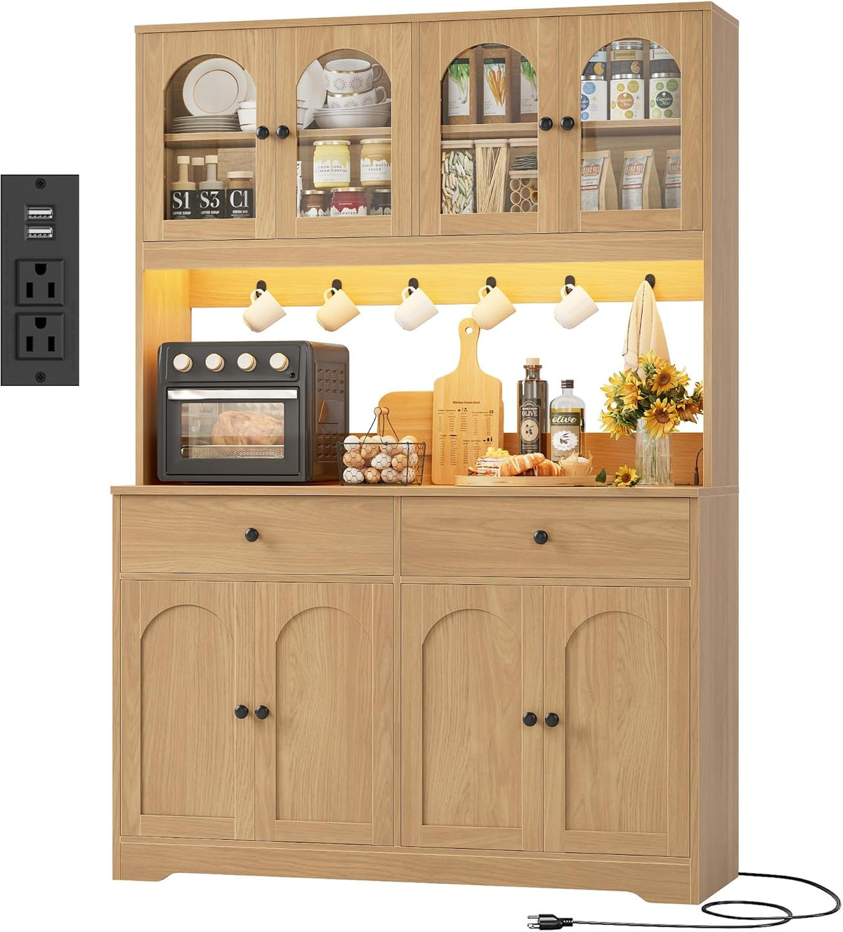Front view of a light wood pantry hutch with four arched glass upper doors, lit countertop and styled counter items.