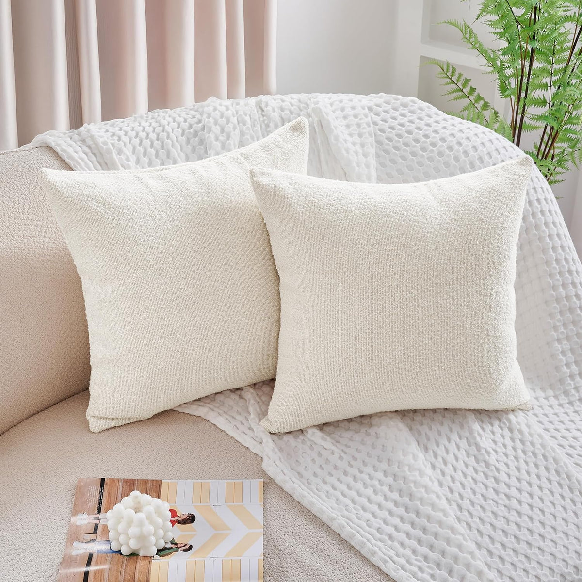 Pair of ivory boucle pillow covers on a beige sofa with a white textured throw