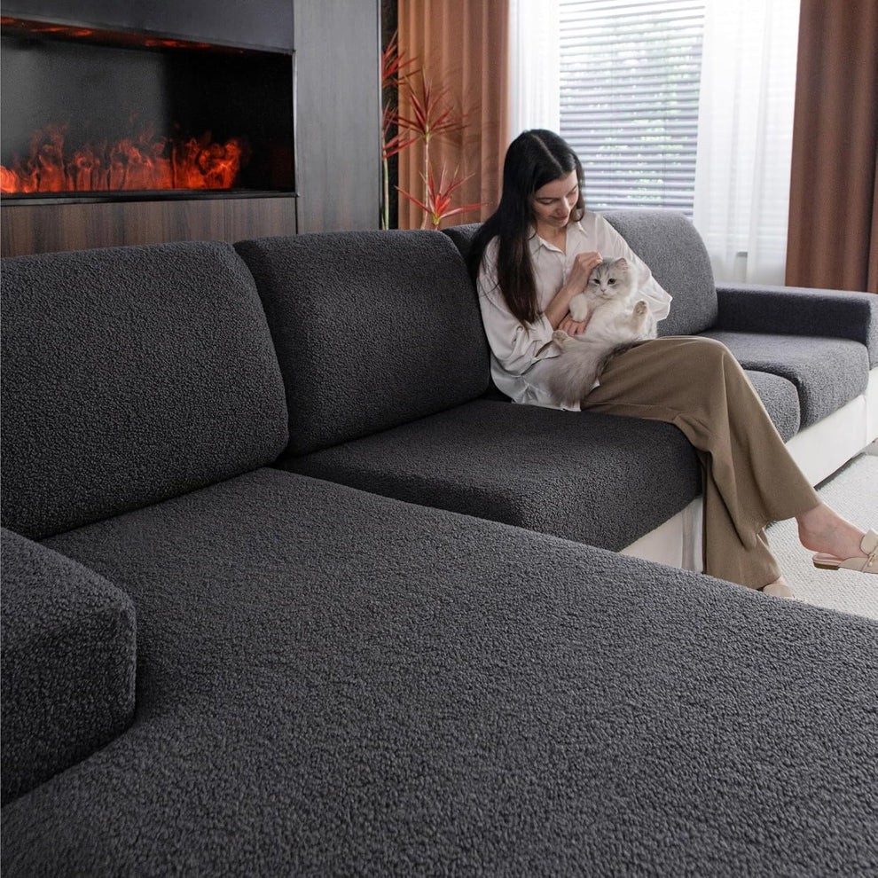 Dark gray textured slipcovers on a sectional with a woman holding a fluffy cat on one seat.