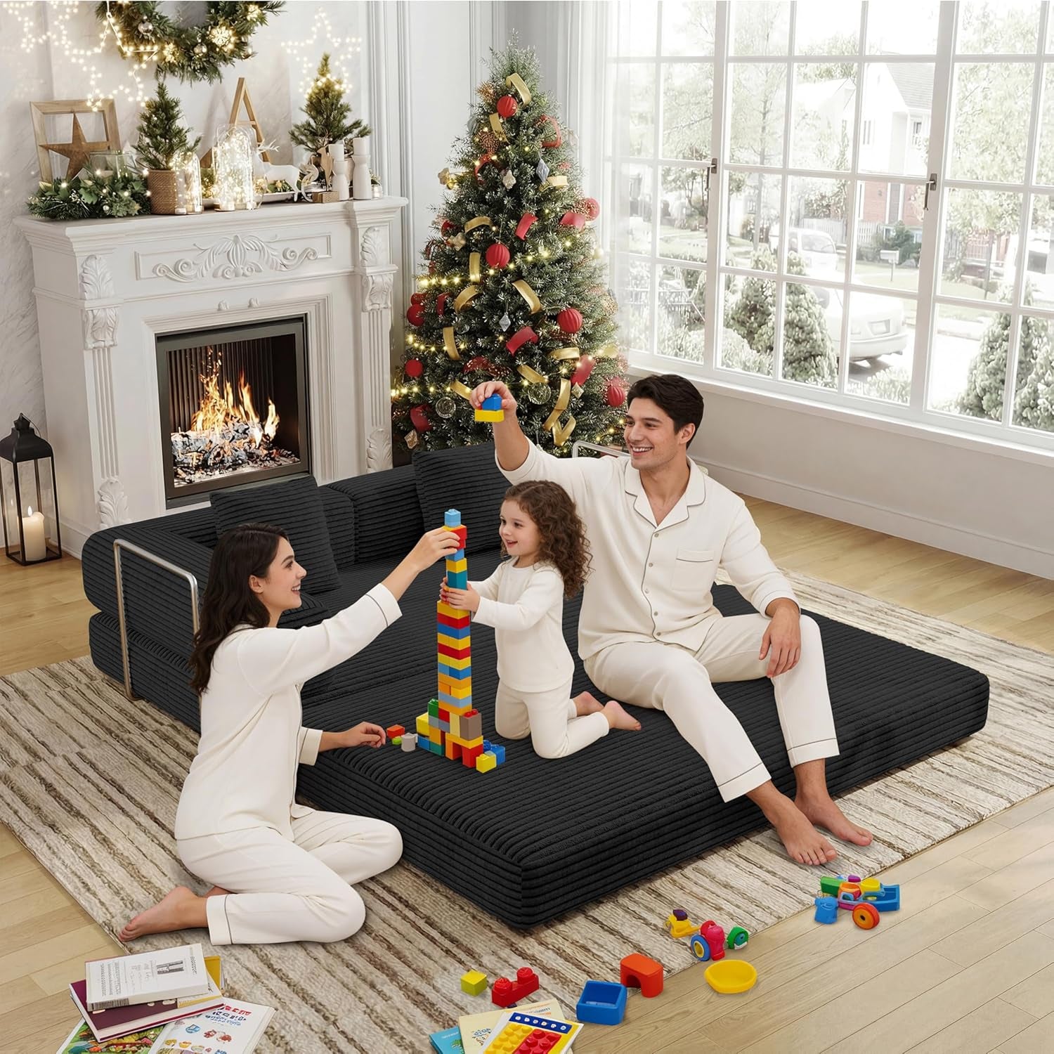 Family playing on a fully flattened black corduroy floor sofa bed in front of a decorated fireplace and Christmas tree.