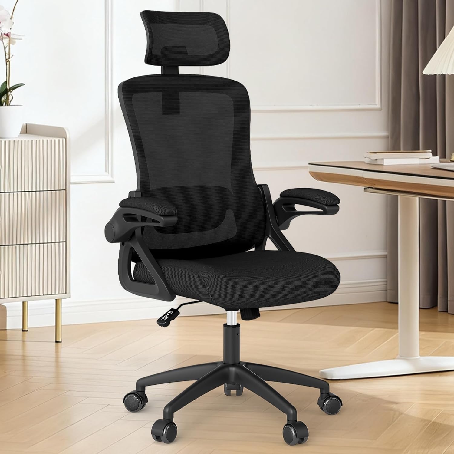 Front three-quarter view of a black mesh office chair with headrest in a light home office setting.