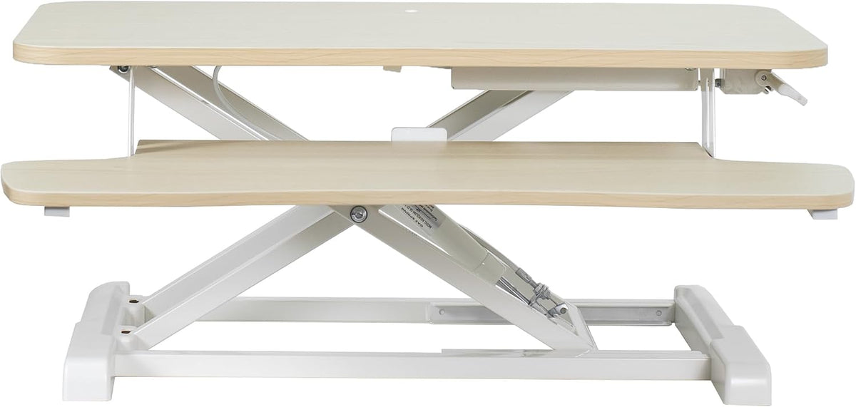 Side profile of a light wood two-tier standing desk converter showing X-frame lift mechanism
