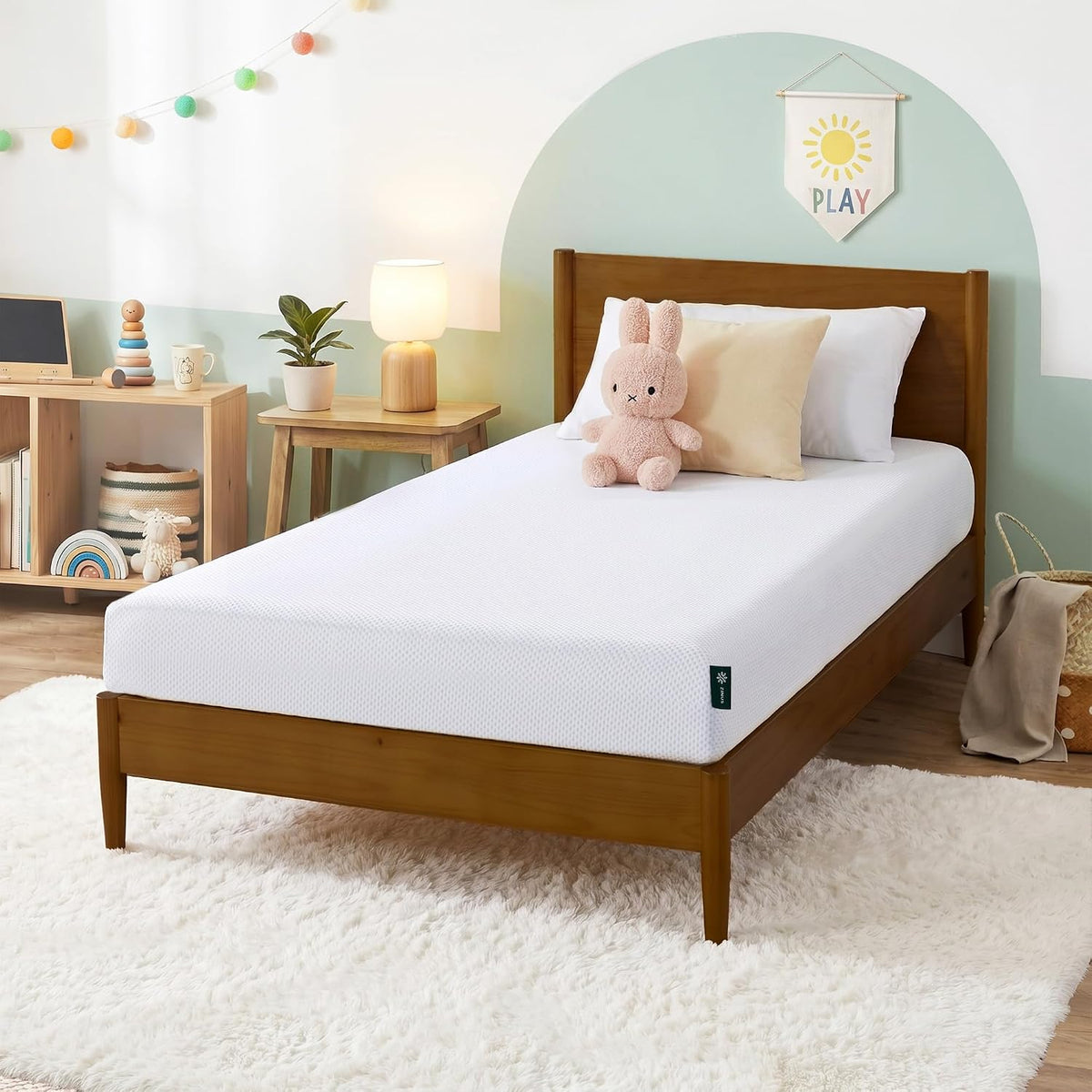 Single white mattress on a wooden twin bed frame in a bright kids' room with plush bunny and bedside lamp