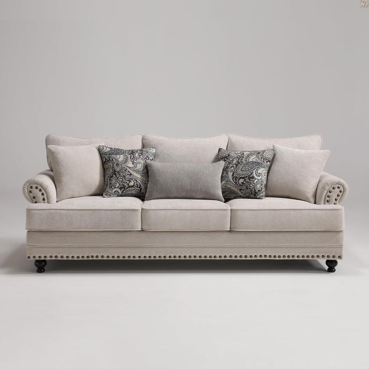 Straight-on view of a three-seat beige sofa with rolled arms, paisley and solid accent pillows, and dark turned legs.