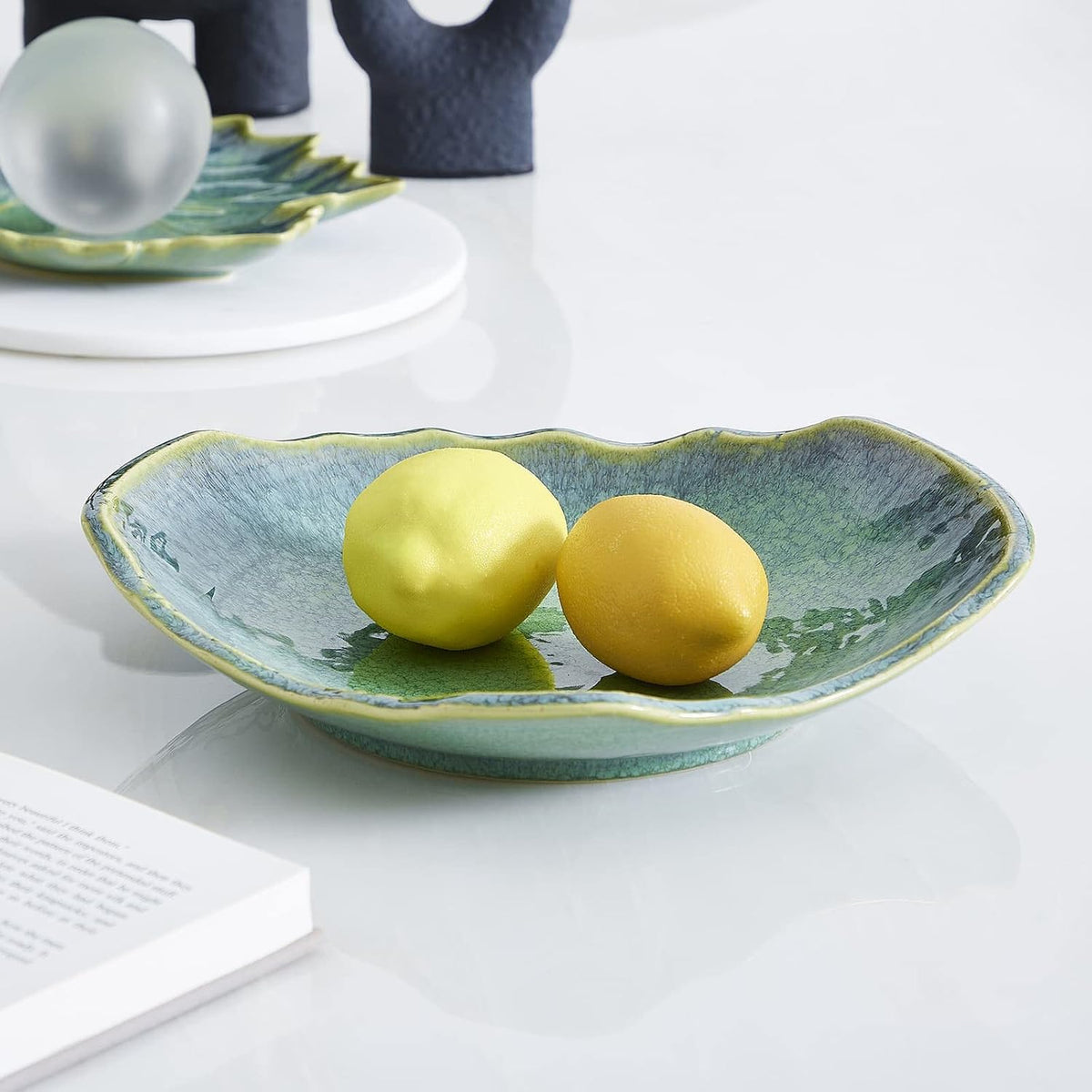 Angled tabletop view of the shallow green bowl holding two yellow fruit pieces on a glossy white surface