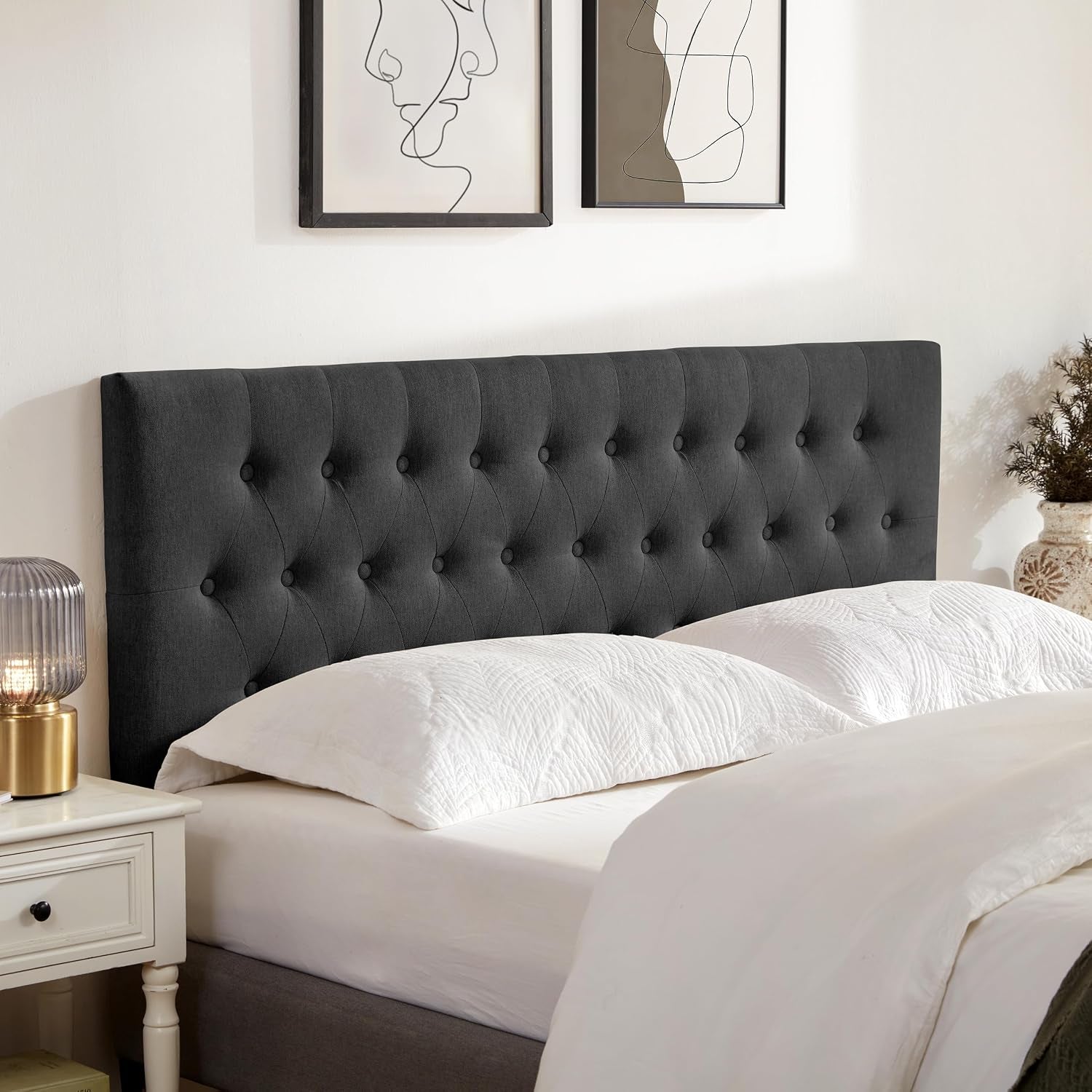 Charcoal tufted queen headboard against a wall with two minimalist line-art frames above the bed.