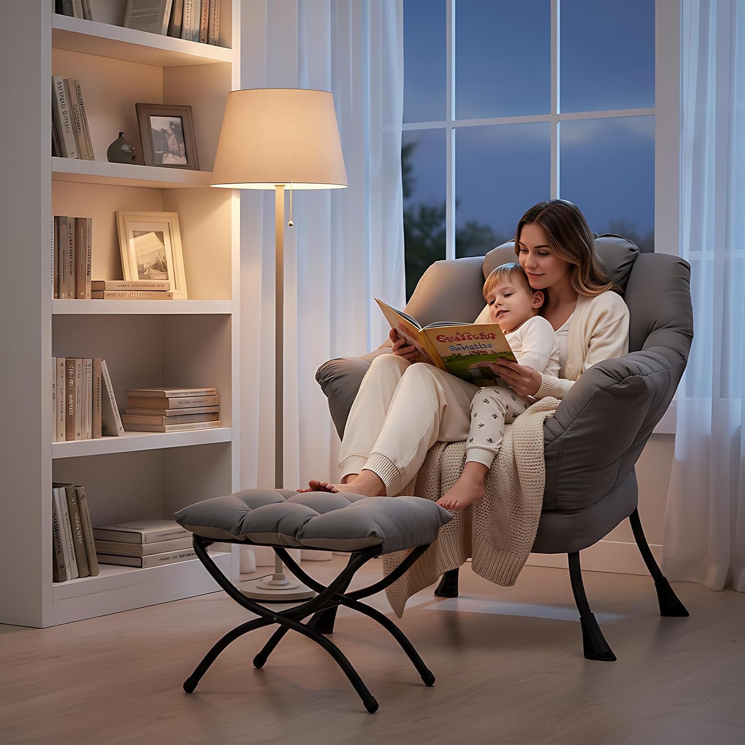 Woman and child reading in a dark grey plush lounge chair with matching ottoman by a lit floor lamp.