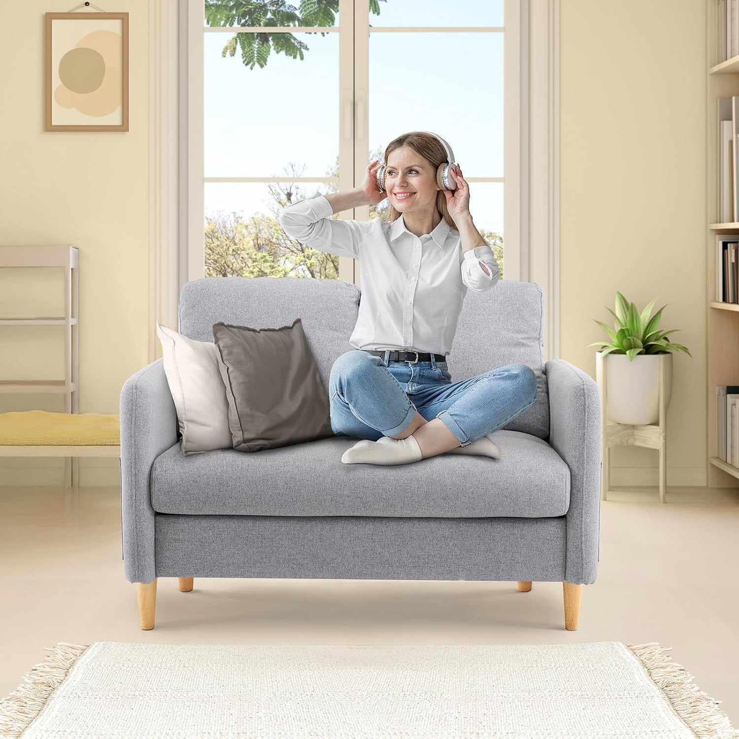 Front view of light-gray two-seat sofa in a bright room with a woman sitting cross-legged wearing headphones.