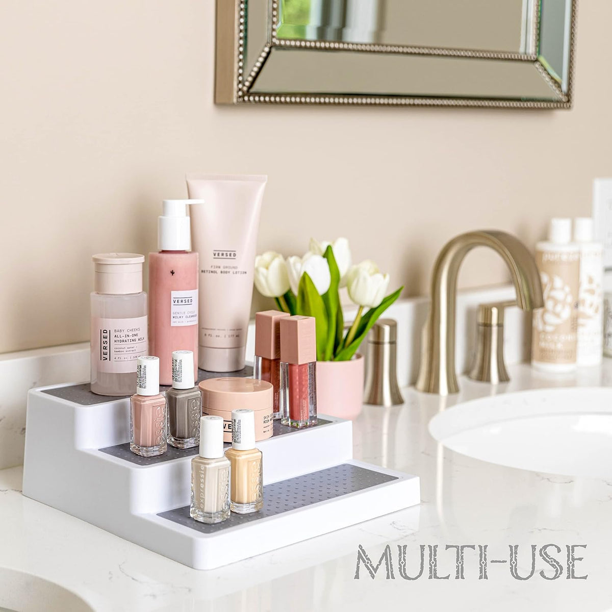 White 3-tier rack on a bathroom counter holding cosmetics and nail polish beside a sink and mirror
