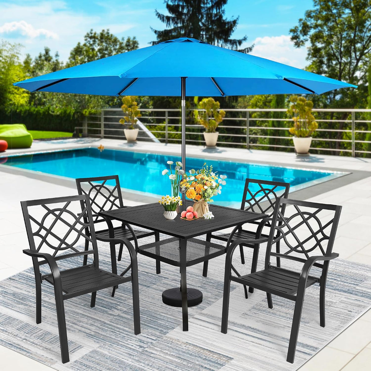 Black metal square table and four matching chairs under a large bright blue patio umbrella, floral centerpiece on table