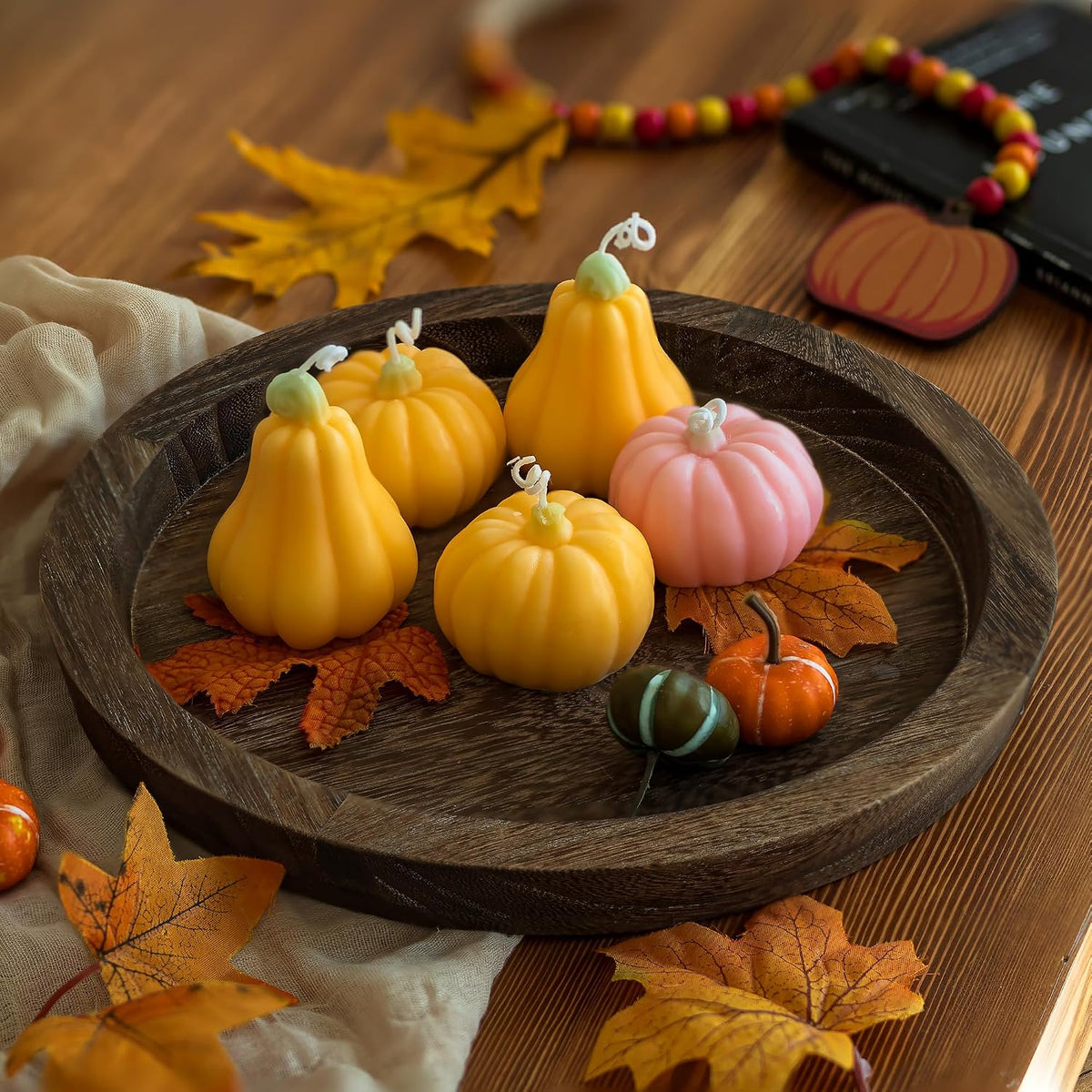 Round wooden tray filled with small decorative pumpkin-shaped candles and autumn leaves on a table
