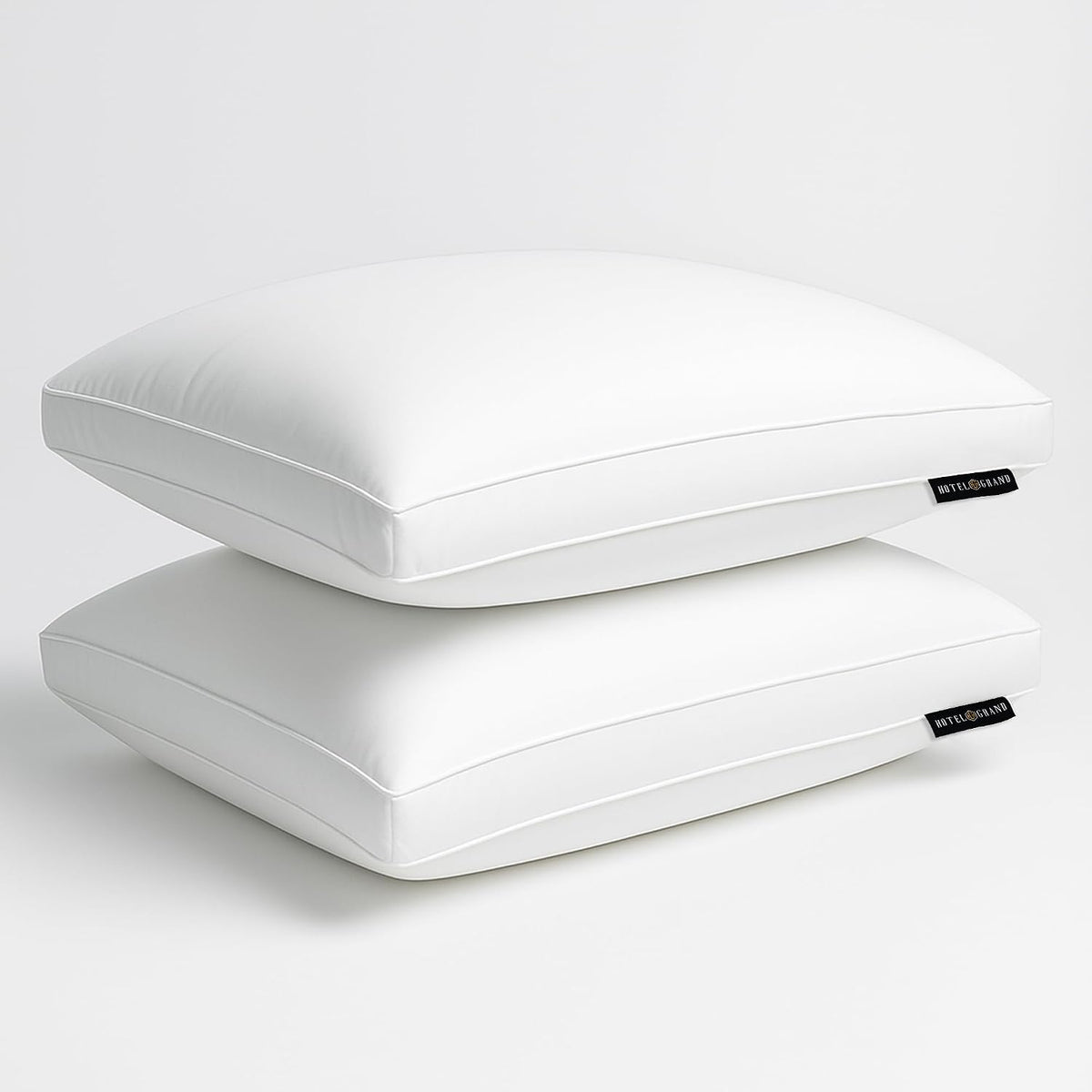 Two white pillows stacked on a reflective surface with small black brand tags visible.