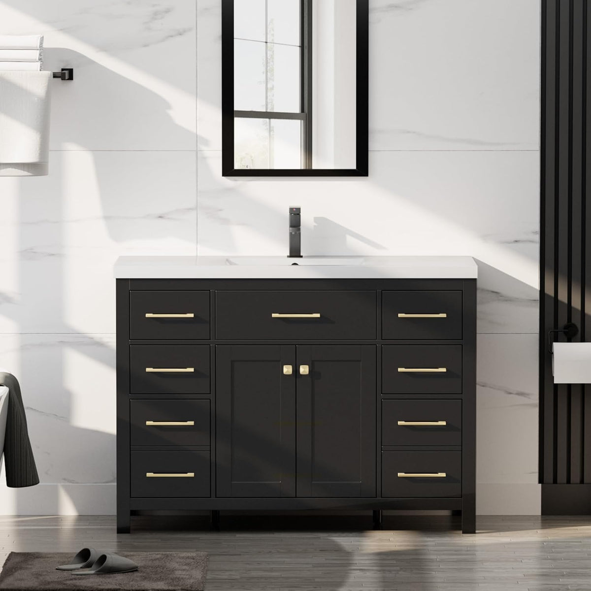 Front view of a black bathroom vanity with white countertop, single faucet and gold drawer pulls.