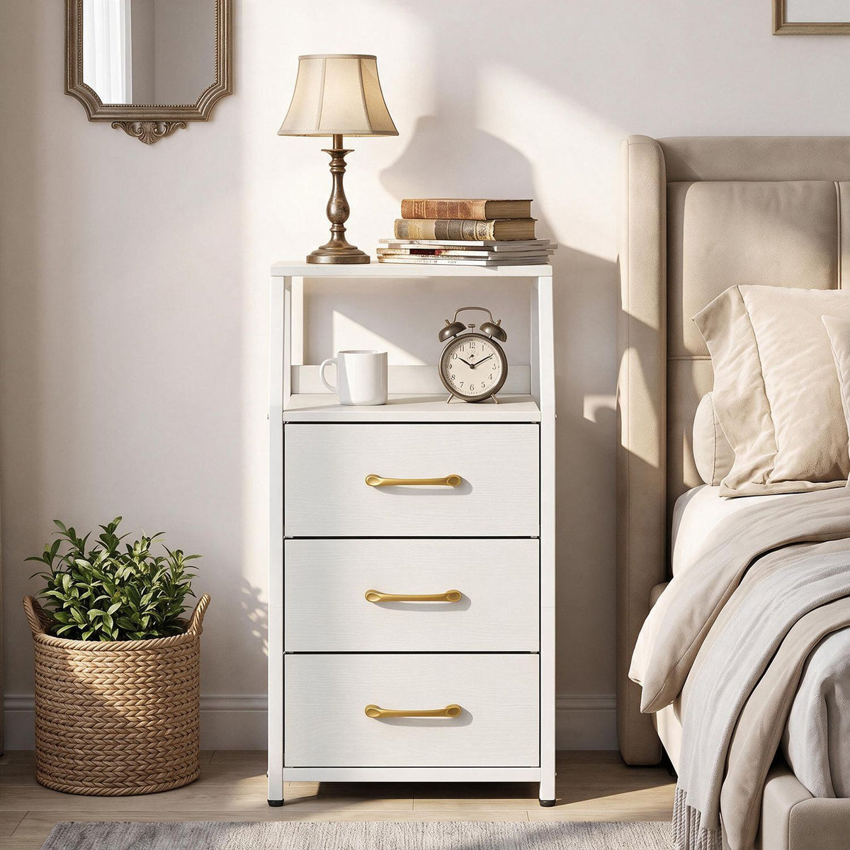White nightstand with three gold-handled drawers and open shelves beside a bed, with a lamp and books on top.
