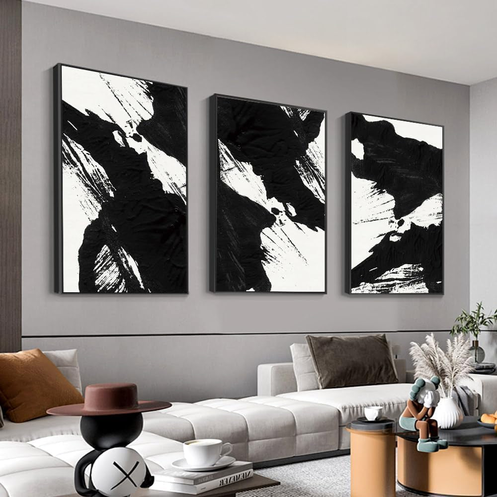 Three vertical black-and-white abstract framed canvases hung above a light-gray sectional with low coffee table and