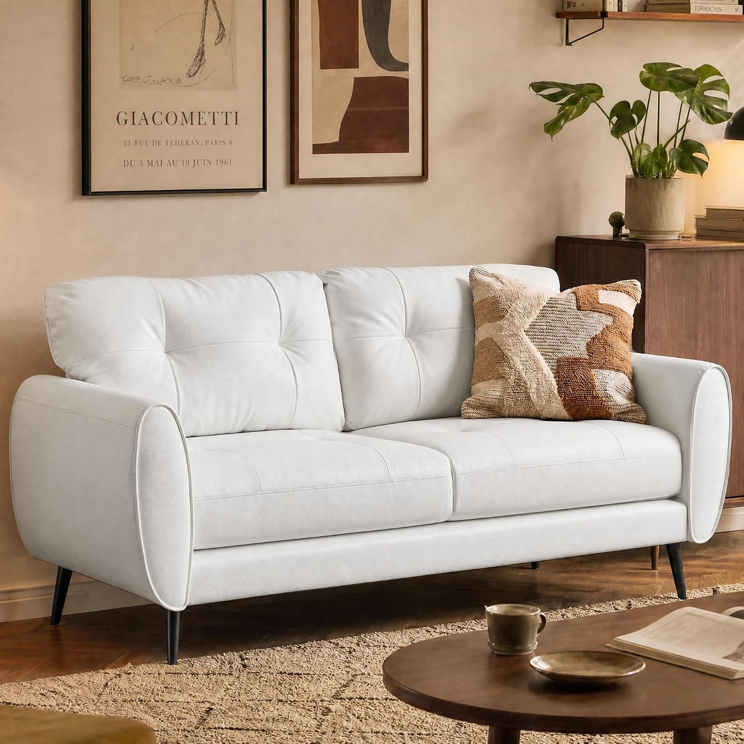 Close side view of a white tufted loveseat with a textured brown-and-cream throw pillow and tapered legs.