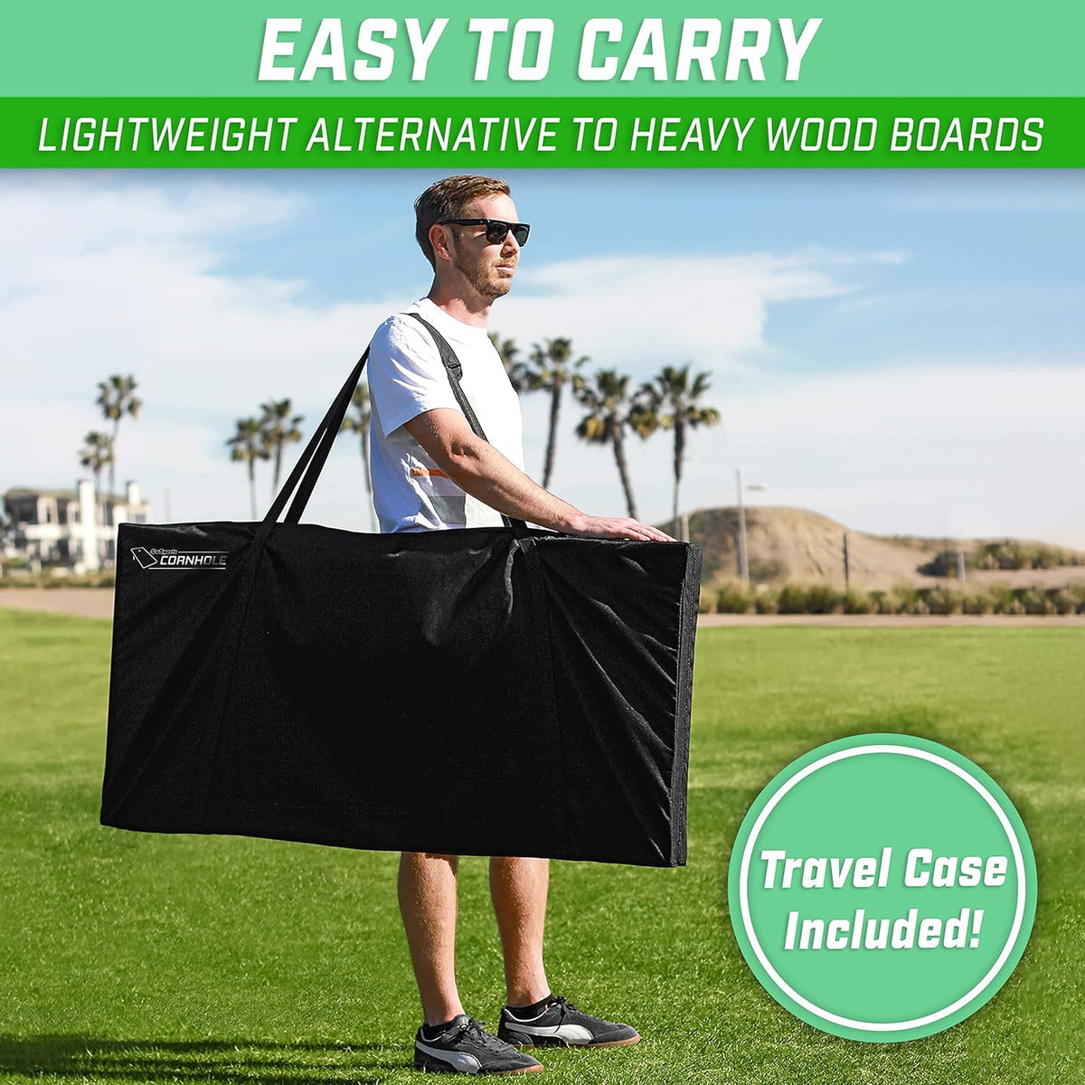 Person carrying folded cornhole boards in a black travel case over one shoulder while walking across grass