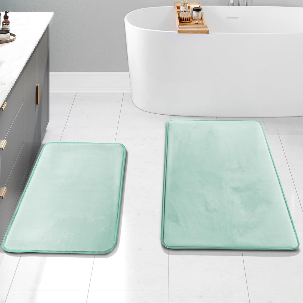 Two rectangular bath mats in mint green placed on a tiled floor beside a bathtub and vanity.