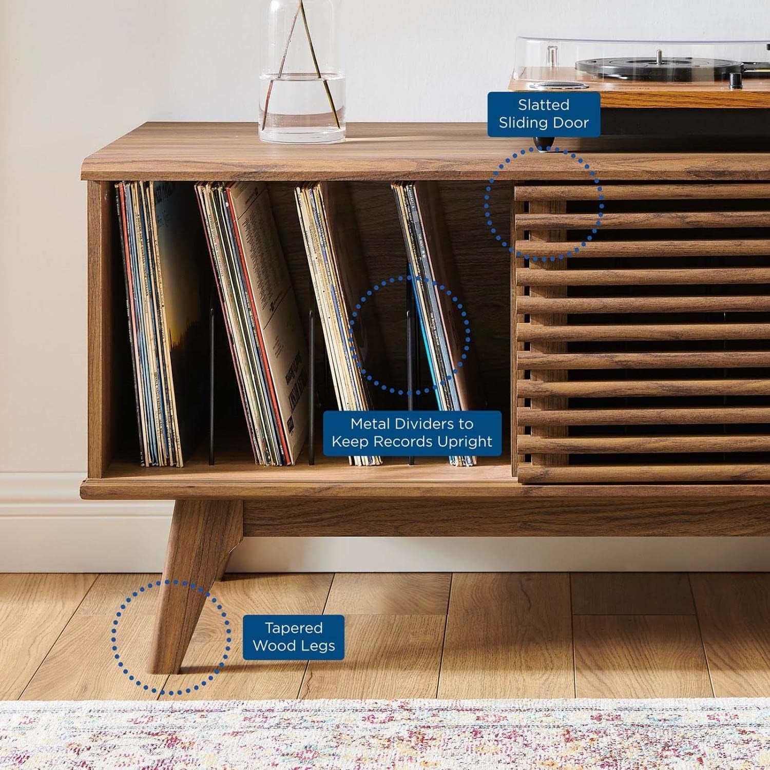 Close view of a walnut-finish record stand showing vertical record slots, slatted sliding door, and tapered wood leg.