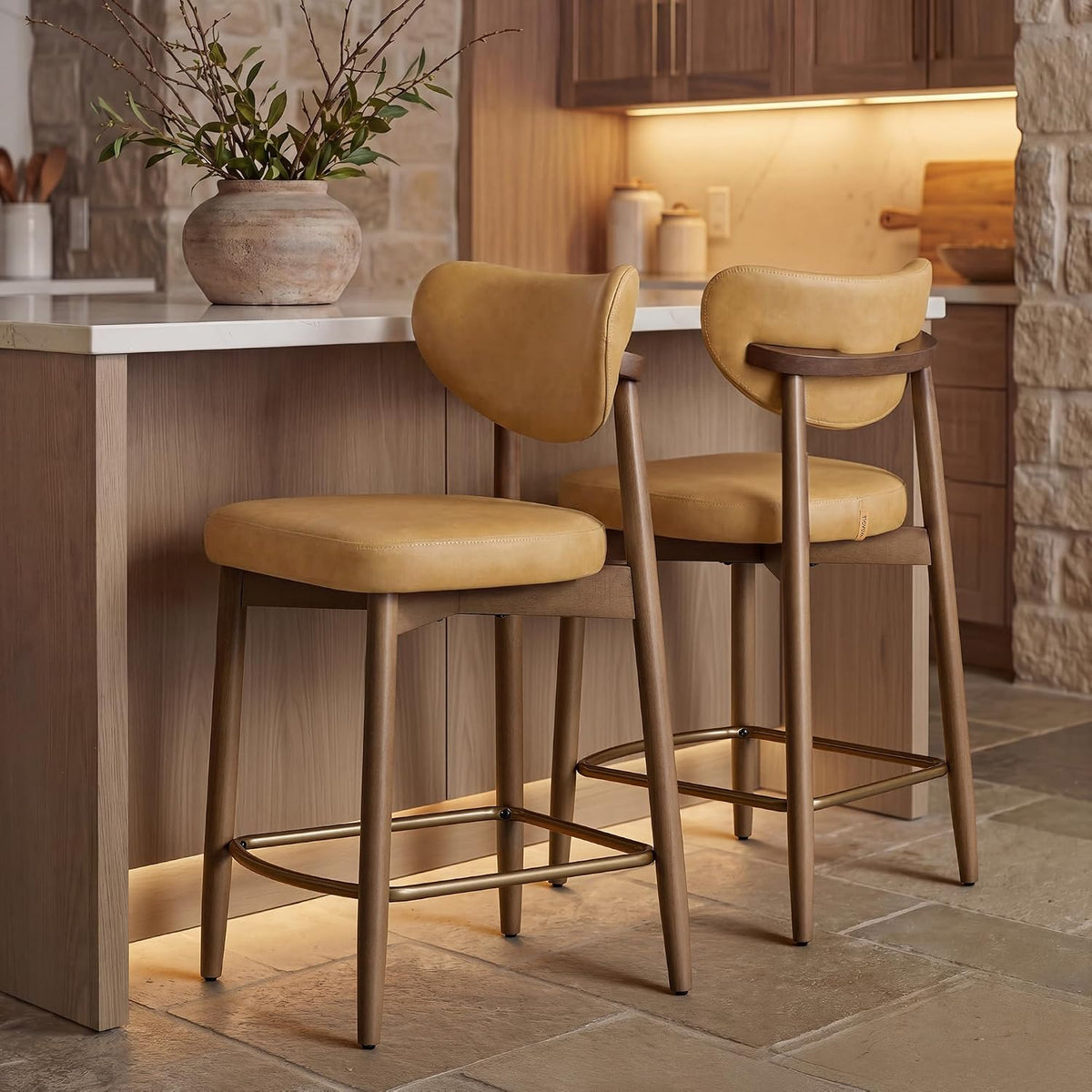 Two tan upholstered bar stools with wooden legs at a kitchen island and a clay vase on the counter.