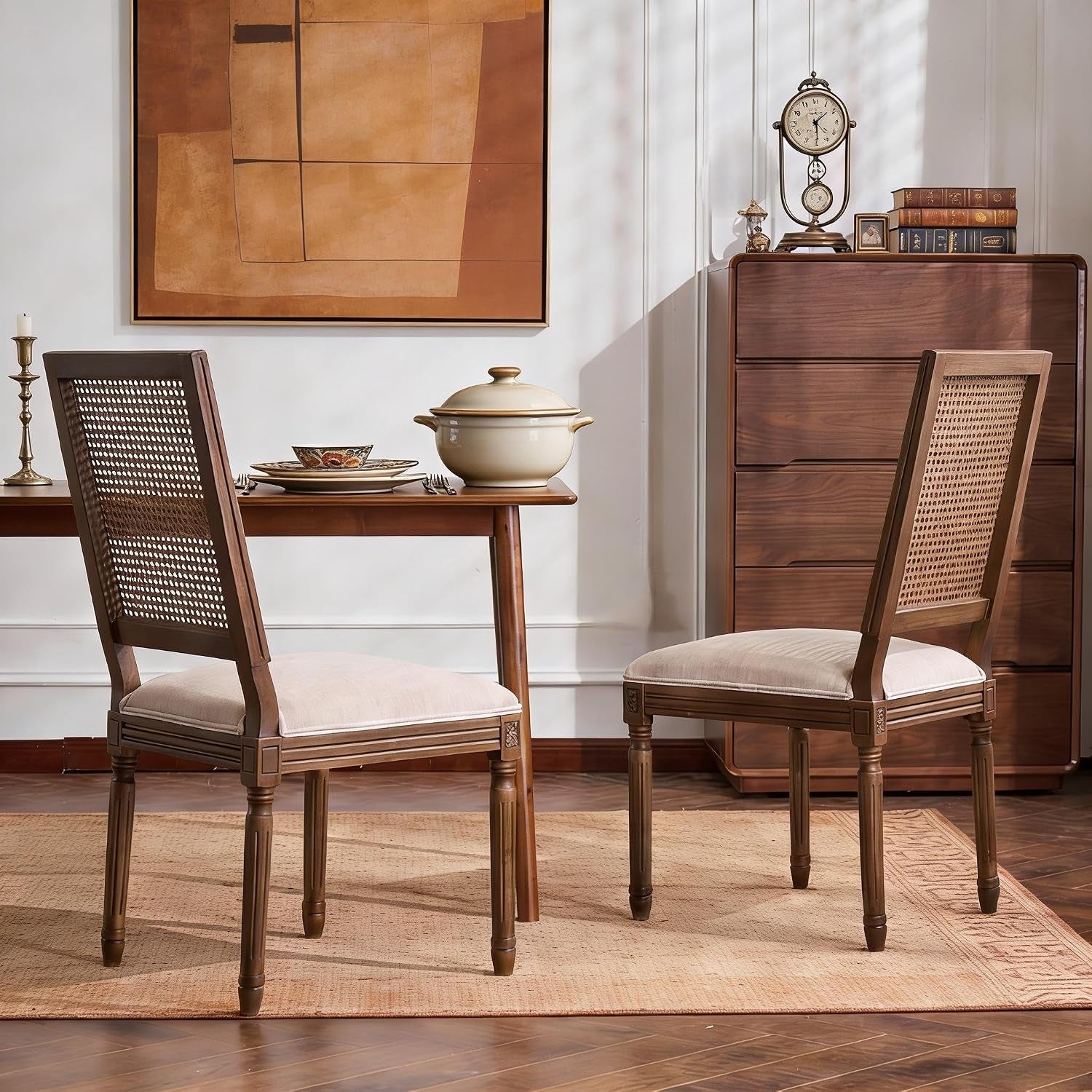 Two armless cane-back dining chairs with beige upholstery beside a wooden table on a woven rug in a warm dining scene
