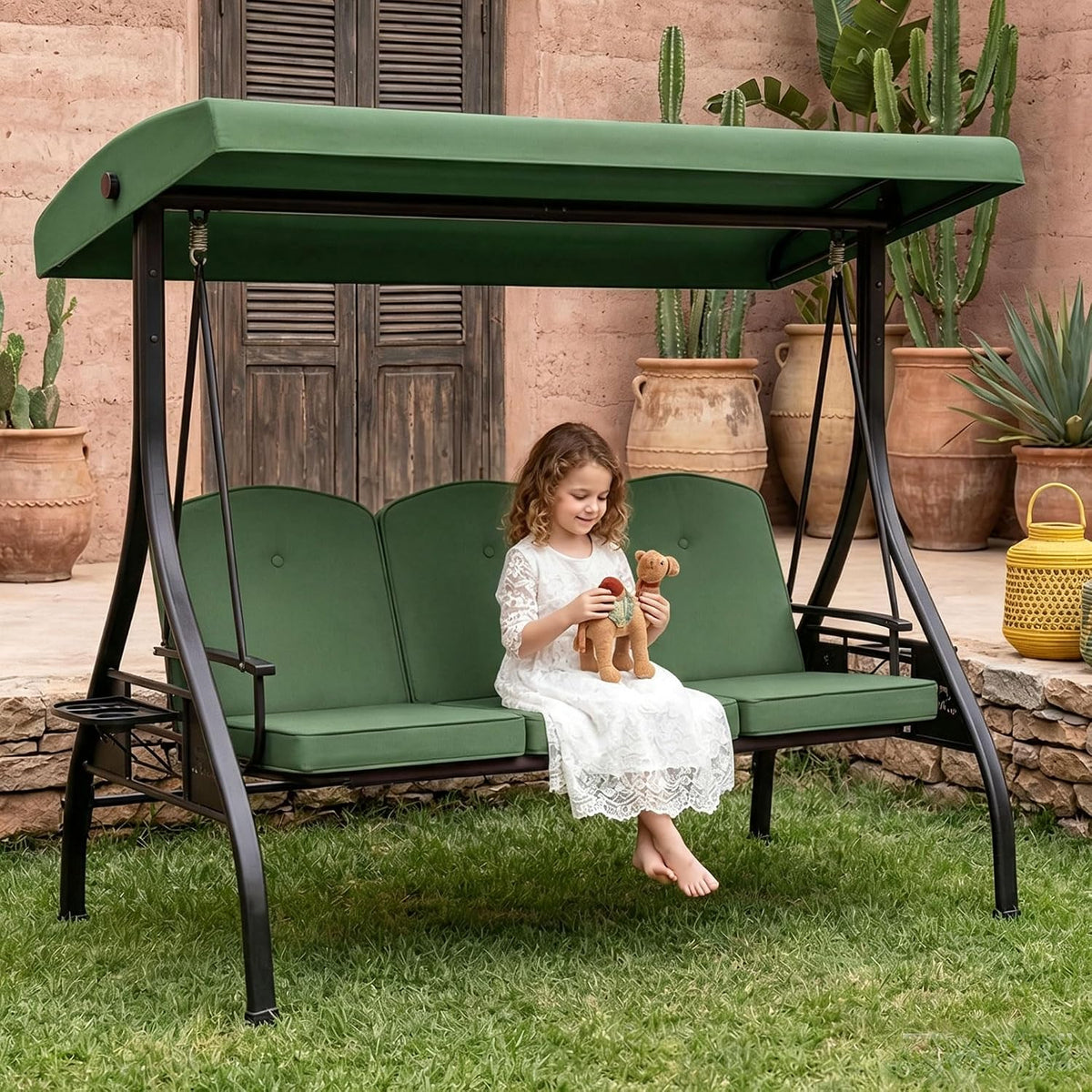 Three-seat outdoor swing with green canopy and cushions; child in white dress sits holding a toy.