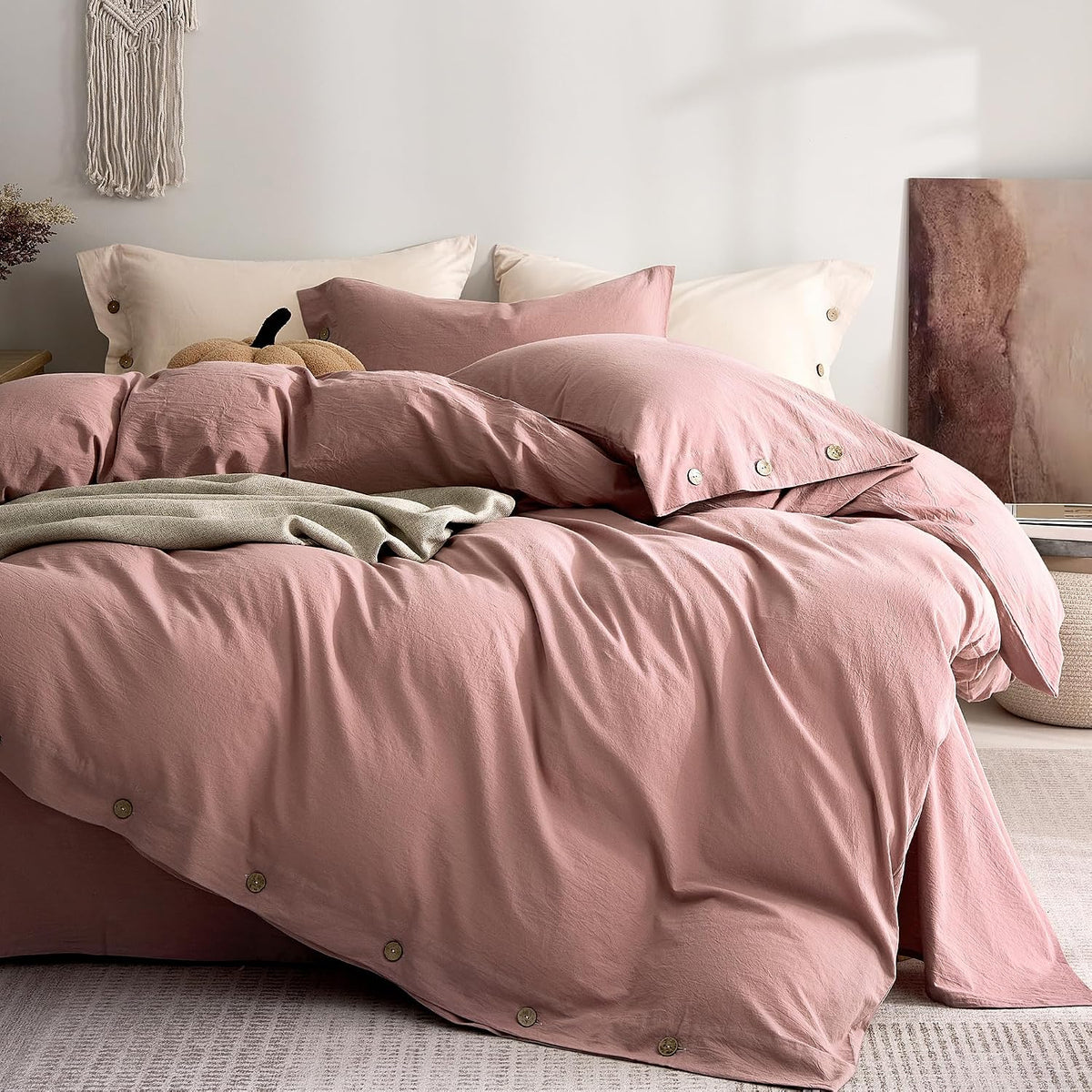Close view of a pink washed-cotton duvet and pillows with wooden artwork at the side.