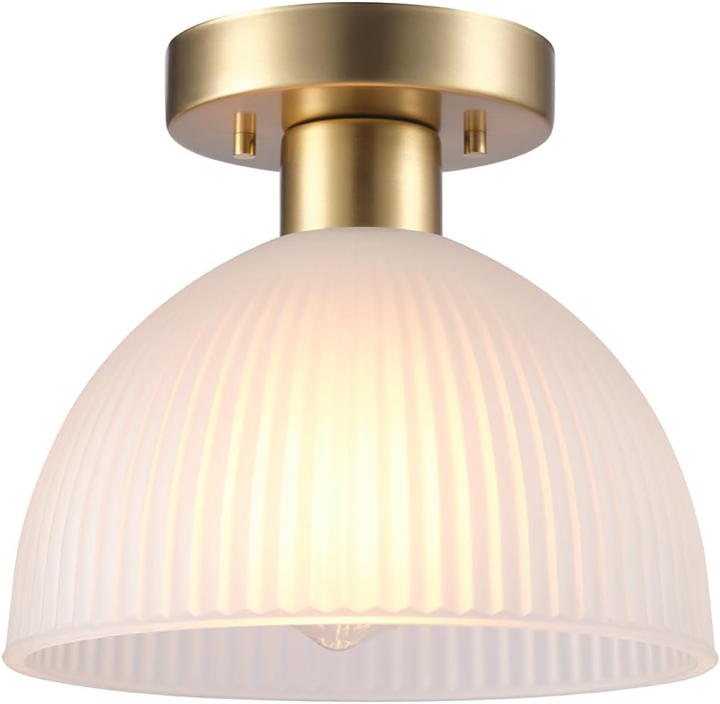 Close-up of a ribbed translucent dome shade glowing warmly, topped by a short matte brass canopy.