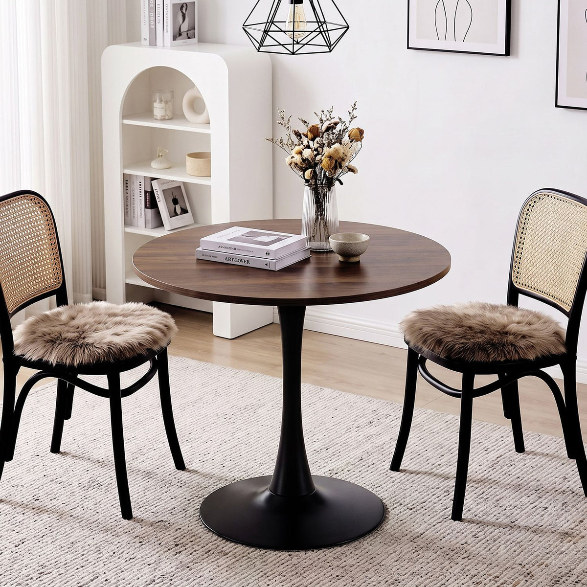 Round walnut-look table with a black pedestal base between two cane-back chairs in a bright dining nook.