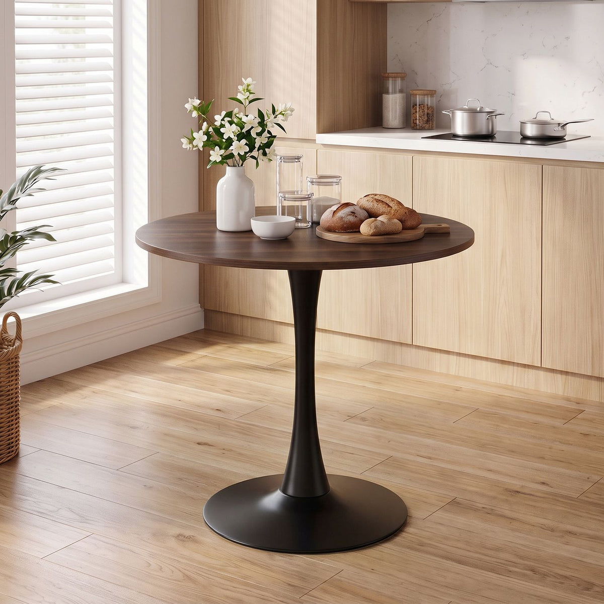 Round dark wood pedestal table styled with flowers and bread in a bright kitchen.