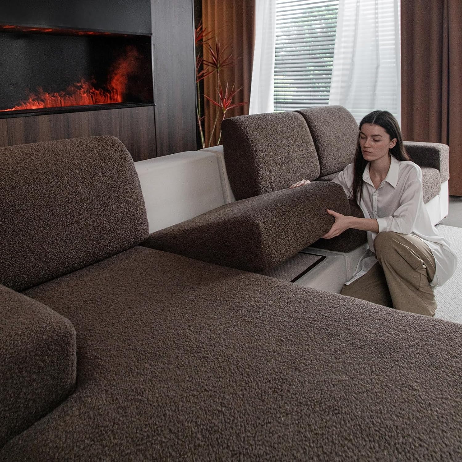 Woman removing a brown slipcovered seat cushion on a sectional to show how the cover fits.