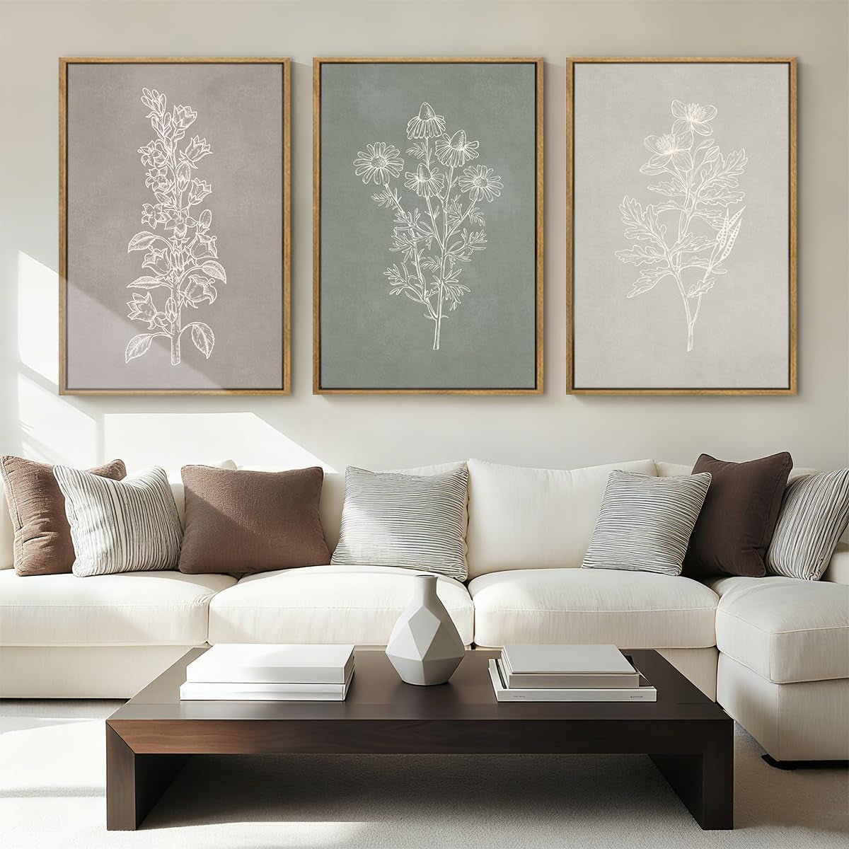 Living room scene with three vertical botanical line-drawings in wood frames hung above a cream sectional sofa.