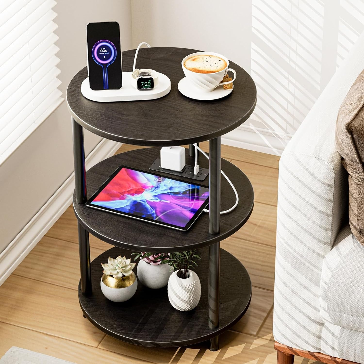 Three-tier round side table in dark rustic brown next to a sofa with coffee, tablet, and small plants on shelves