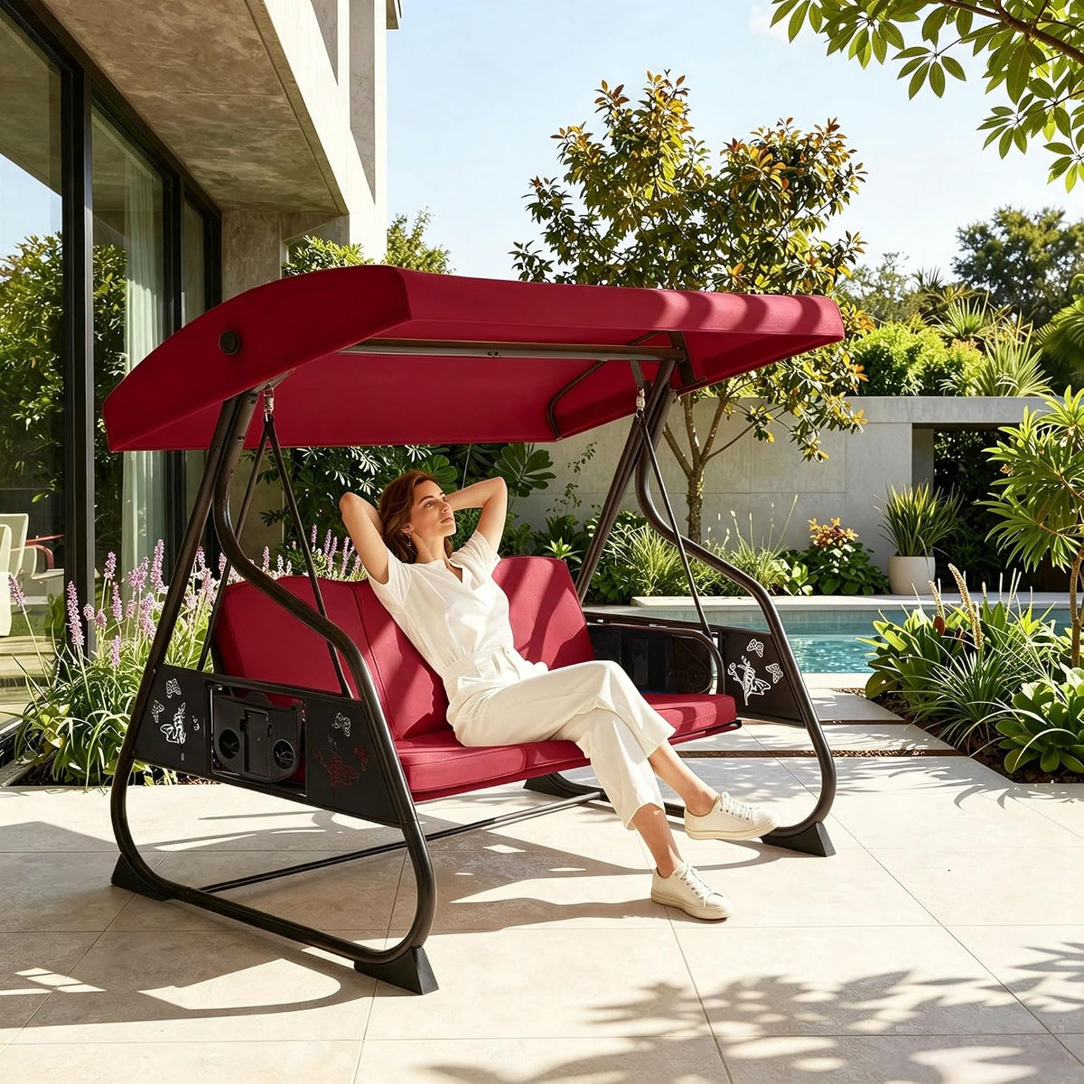 Woman relaxing on a red-cushioned porch swing with matching canopy beside a tiled pool area.