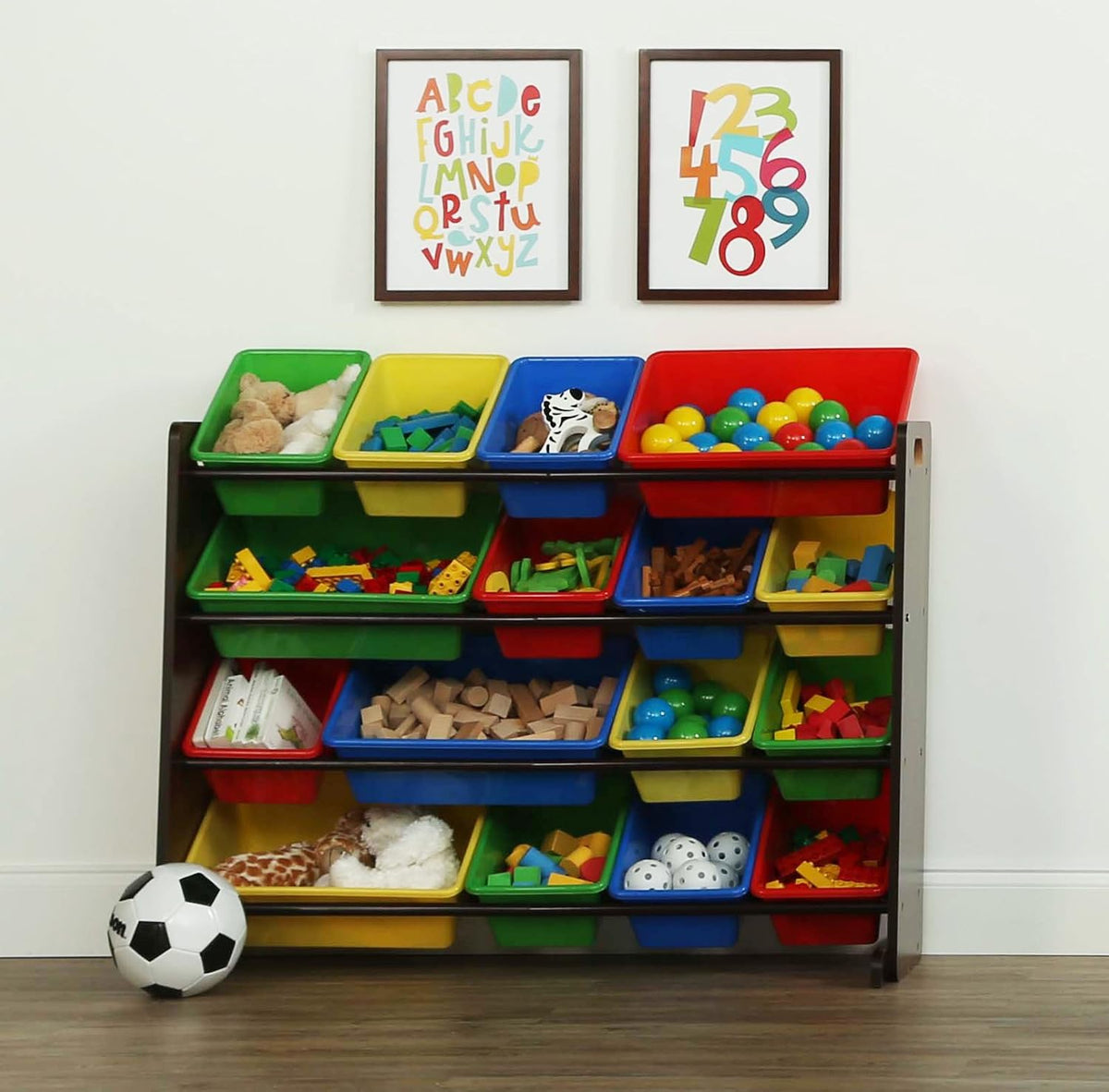 Toy organizer against a wall with framed prints, bins filled with toys and a soccer ball on the floor.