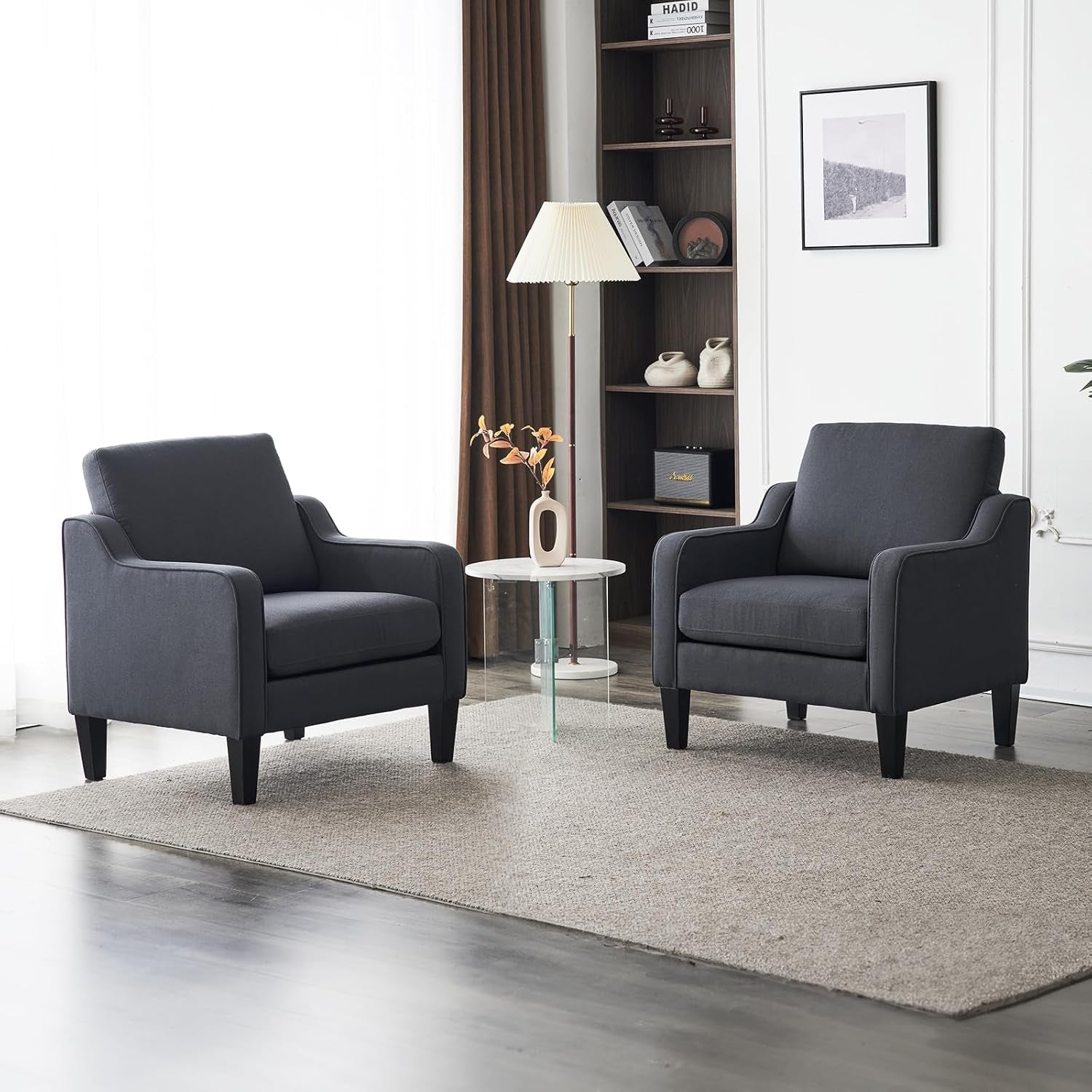Pair of dark gray upholstered mid-century armchairs with black wooden legs in a bright living space.