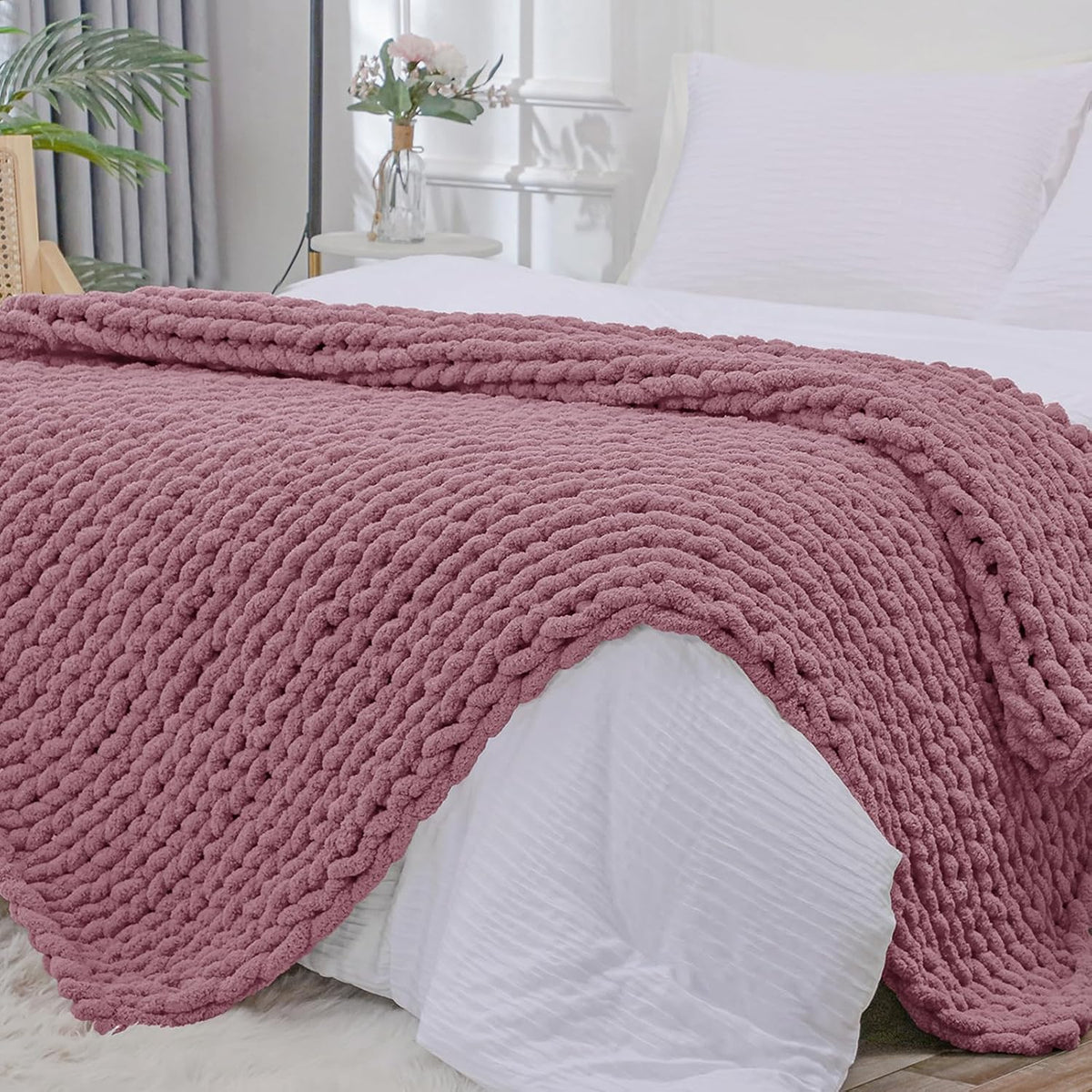 Dusty rose chunky knit throw spread across a white bed, photographed from the foot showing braided rows.