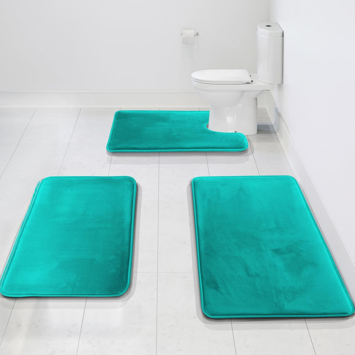 Three bright teal bath rugs on white tile including a U-shaped rug positioned around the toilet