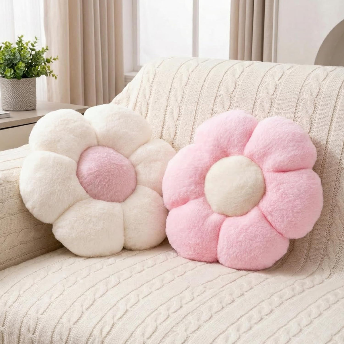 Pink and white daisy-shaped plush throw pillows resting side-by-side on a cream cable-knit sofa