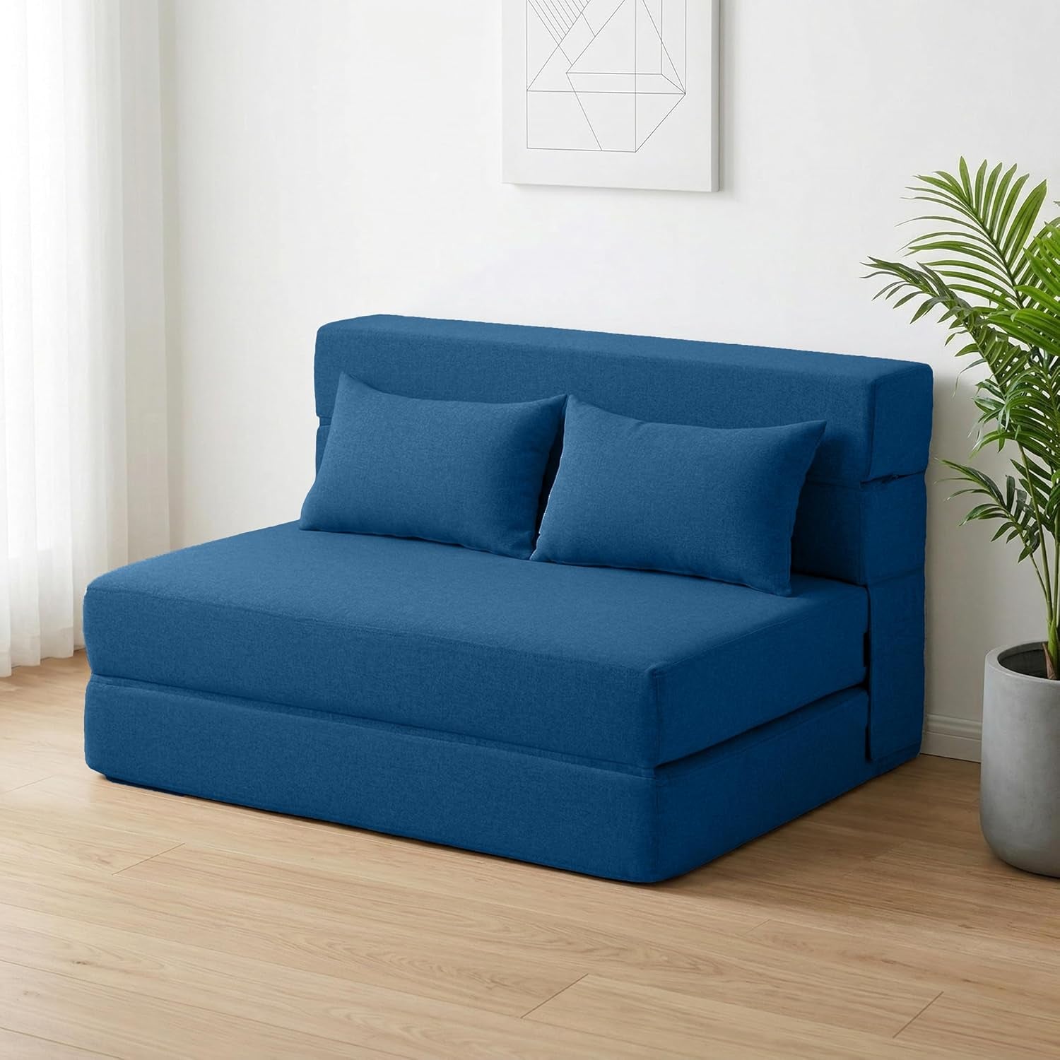 Blue folding twin sofa bed set as a compact sofa with two pillows in a bright room beside a potted plant.