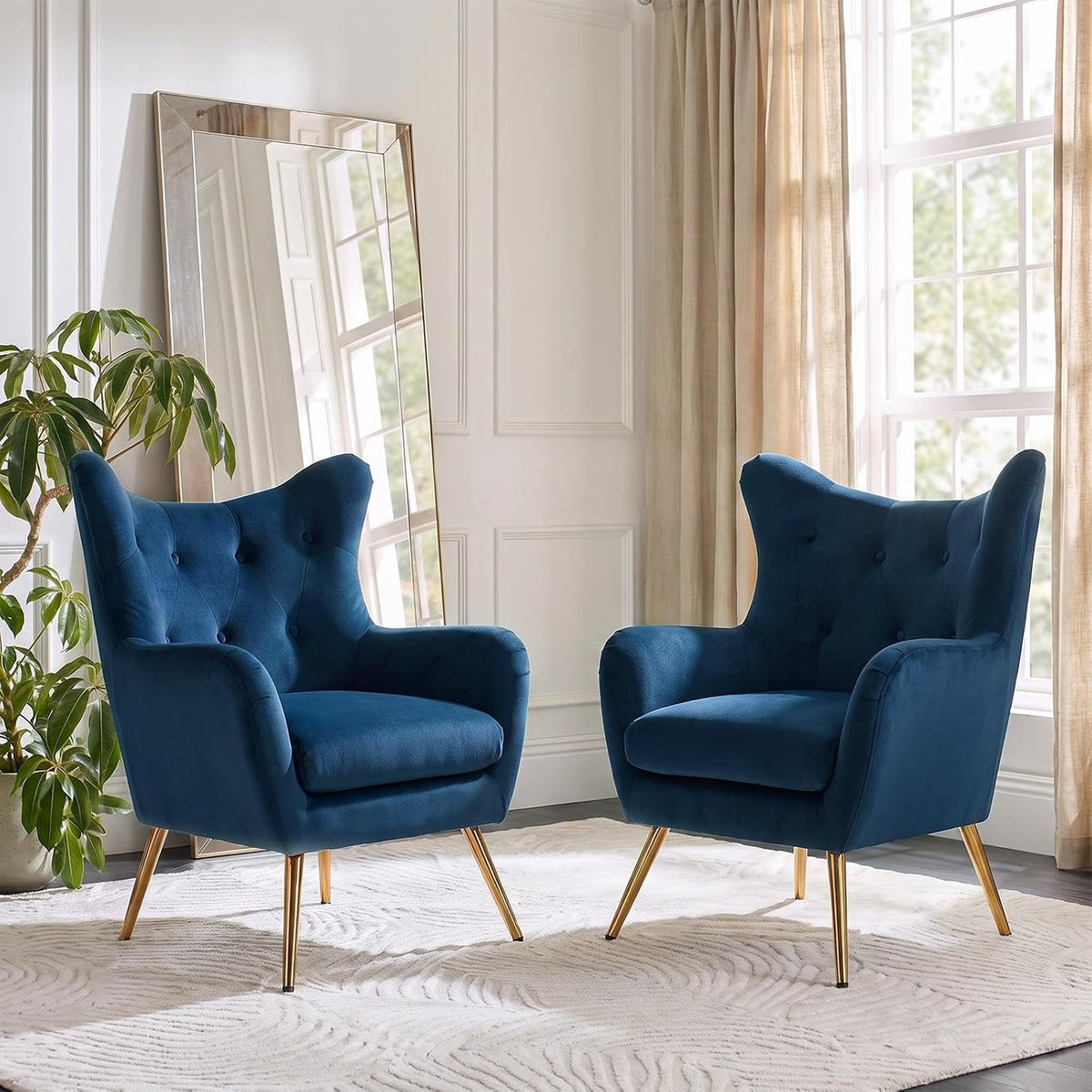 Two blue wingback chairs angled toward each other beside a bright window and plant