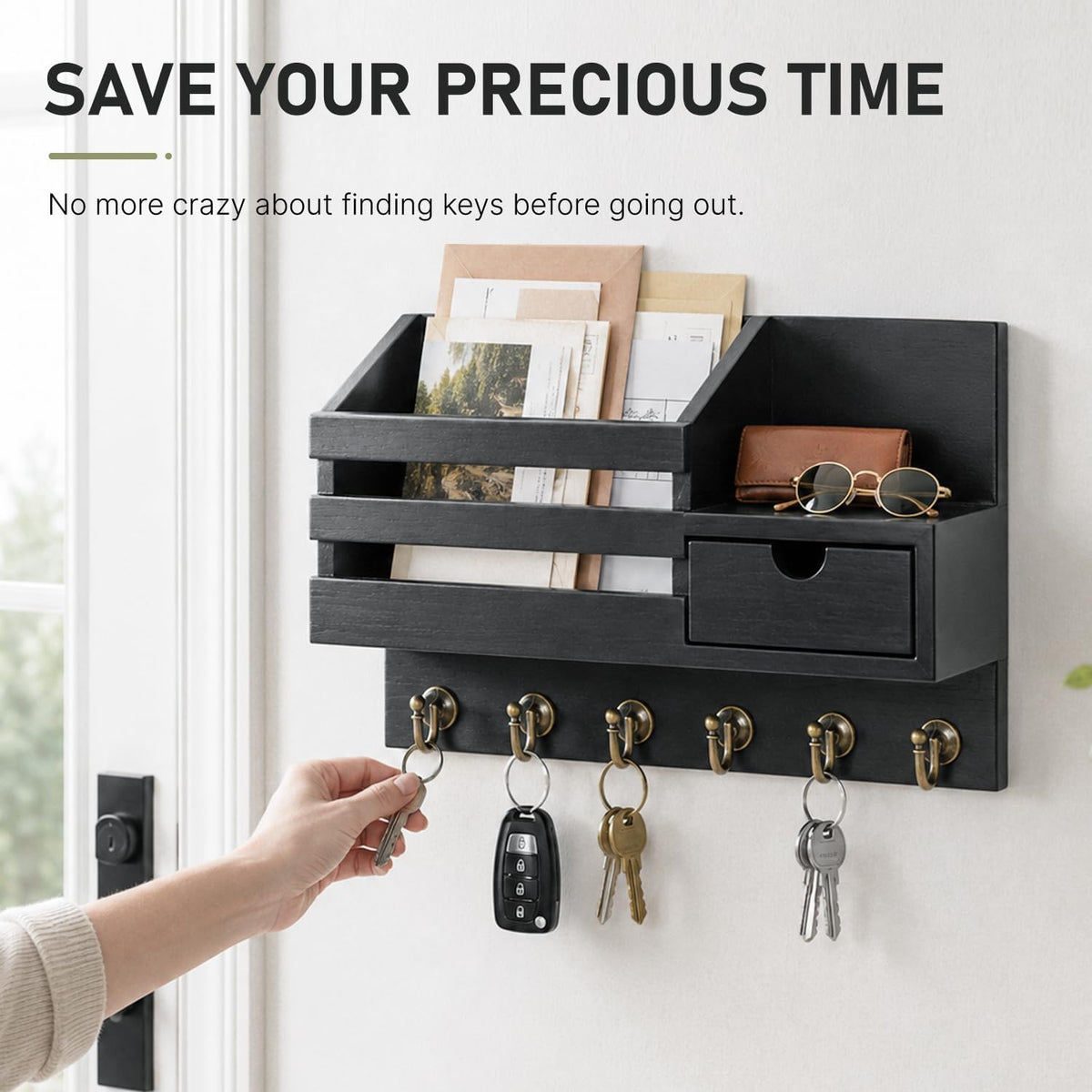 Wall-mounted black organizer with keys hanging and a hand reaching to grab a key from the leftmost hook.