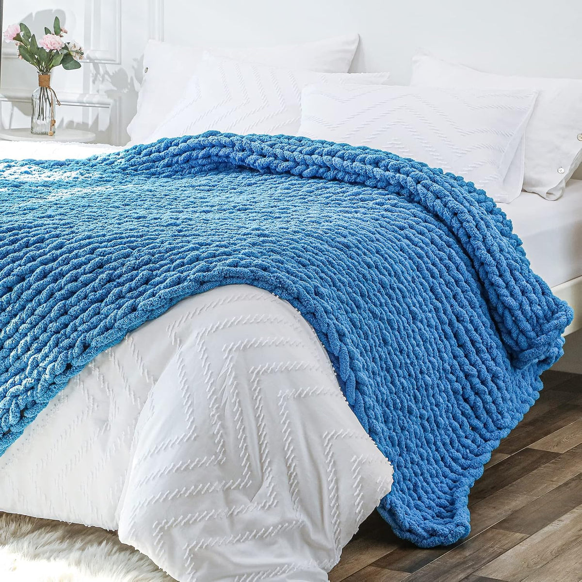 Vibrant sky-blue chunky knit blanket folded across the foot of a white-made bed, edge hanging over mattress.