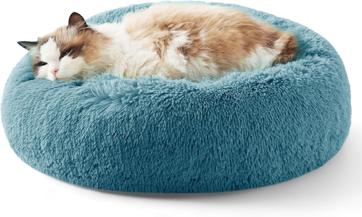 Fluffy cat curled inside a teal round faux-fur donut bed with a raised rim, close side view.