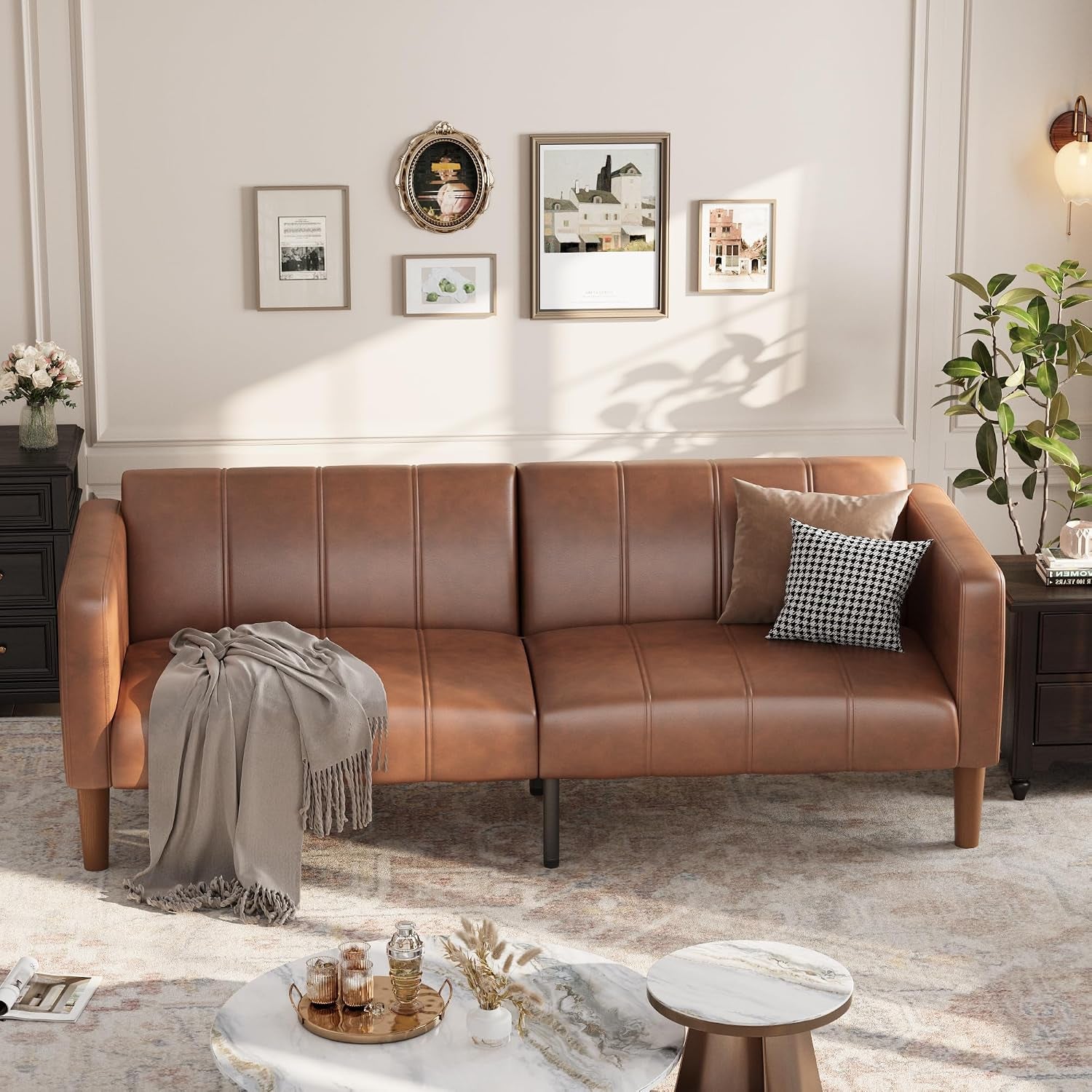 Three‑seat brown faux‑leather futon sofa in a living room with pillows and throw