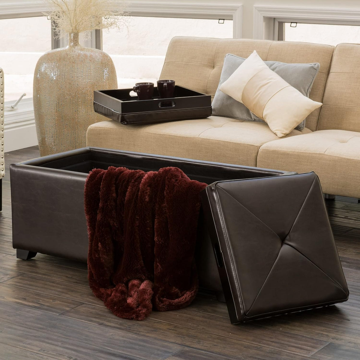 Ottoman lid removed and leaning at the side while a deep red plush throw spills out from the open storage compartment.