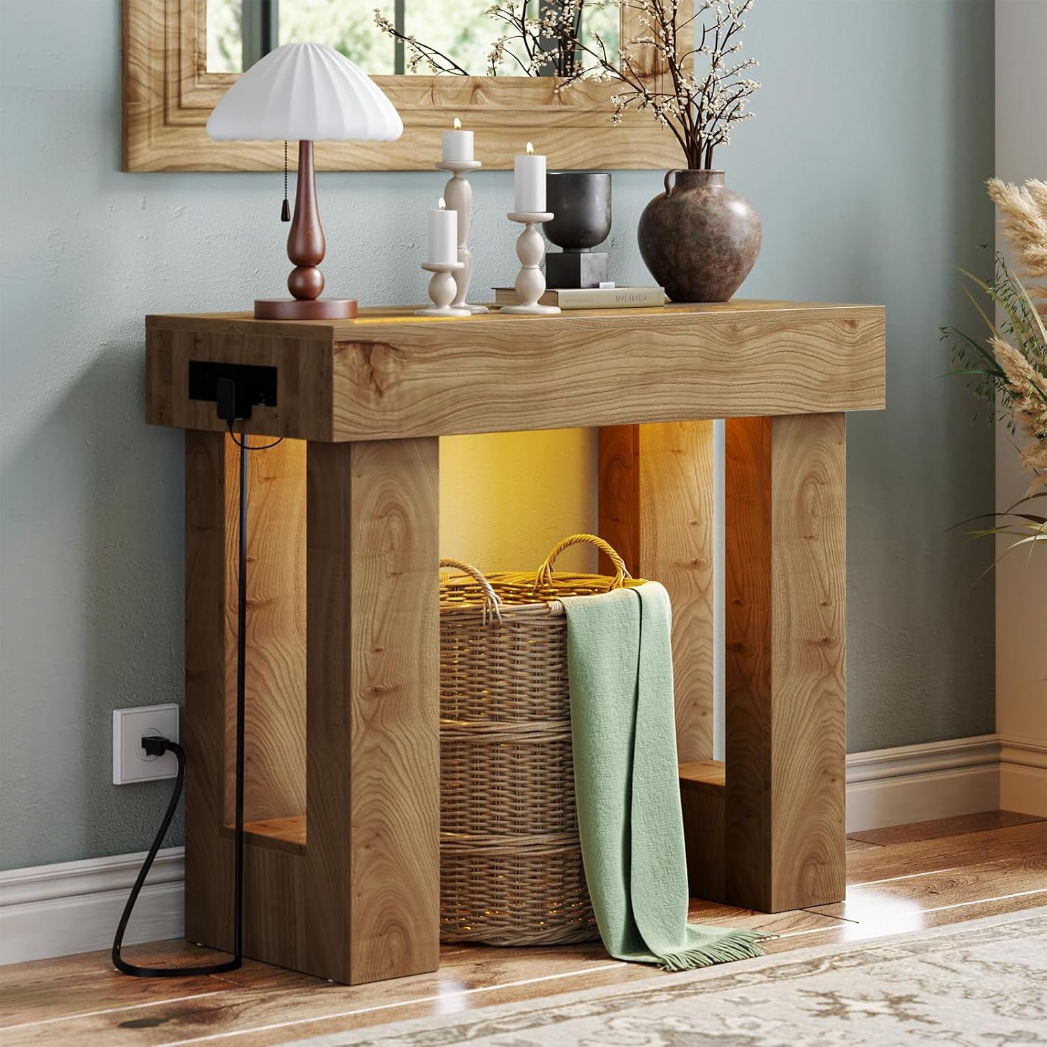 Three-quarter close view of a wooden console with a pleated lamp, three candles, ceramic vase on top and a woven basket